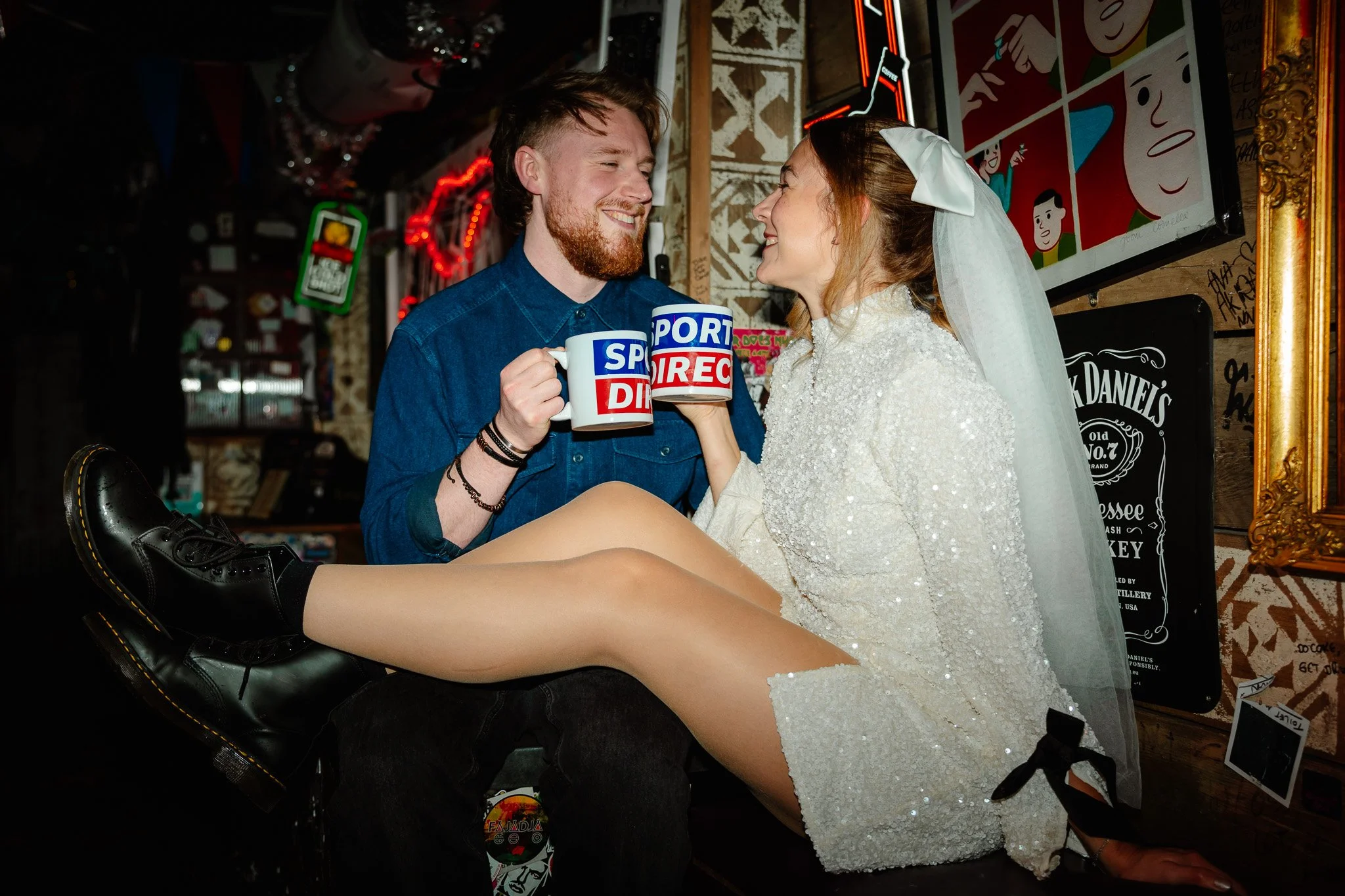 An alternative couple in a dive bar drinking from Sports Direct mugs in Junior Jacksons Manchester. The bride is in a mini dress and dr martens boots.