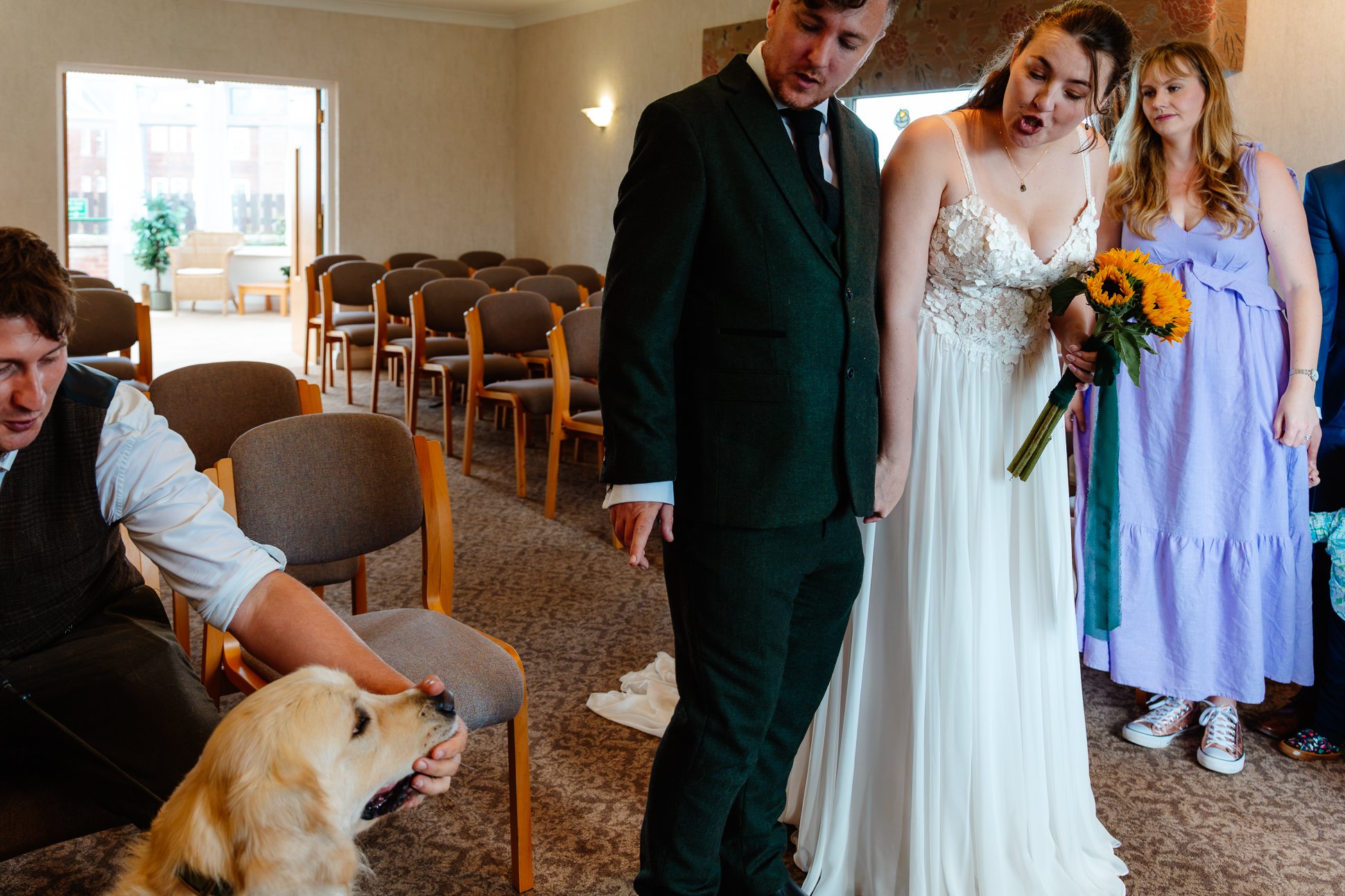 An alternative couple has eloped at Whitby Registry Office with just their friends and their golden retriever. The bride is wearing doc martens and holding sunflowers. The bride is shushing this dog in a funny candid image.