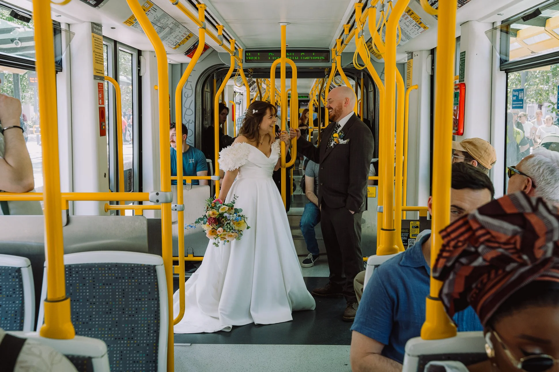 A vibrant colourful photo showing an alternative couple on the tram in Manchester. They have just got married and are in their wedding clothes.