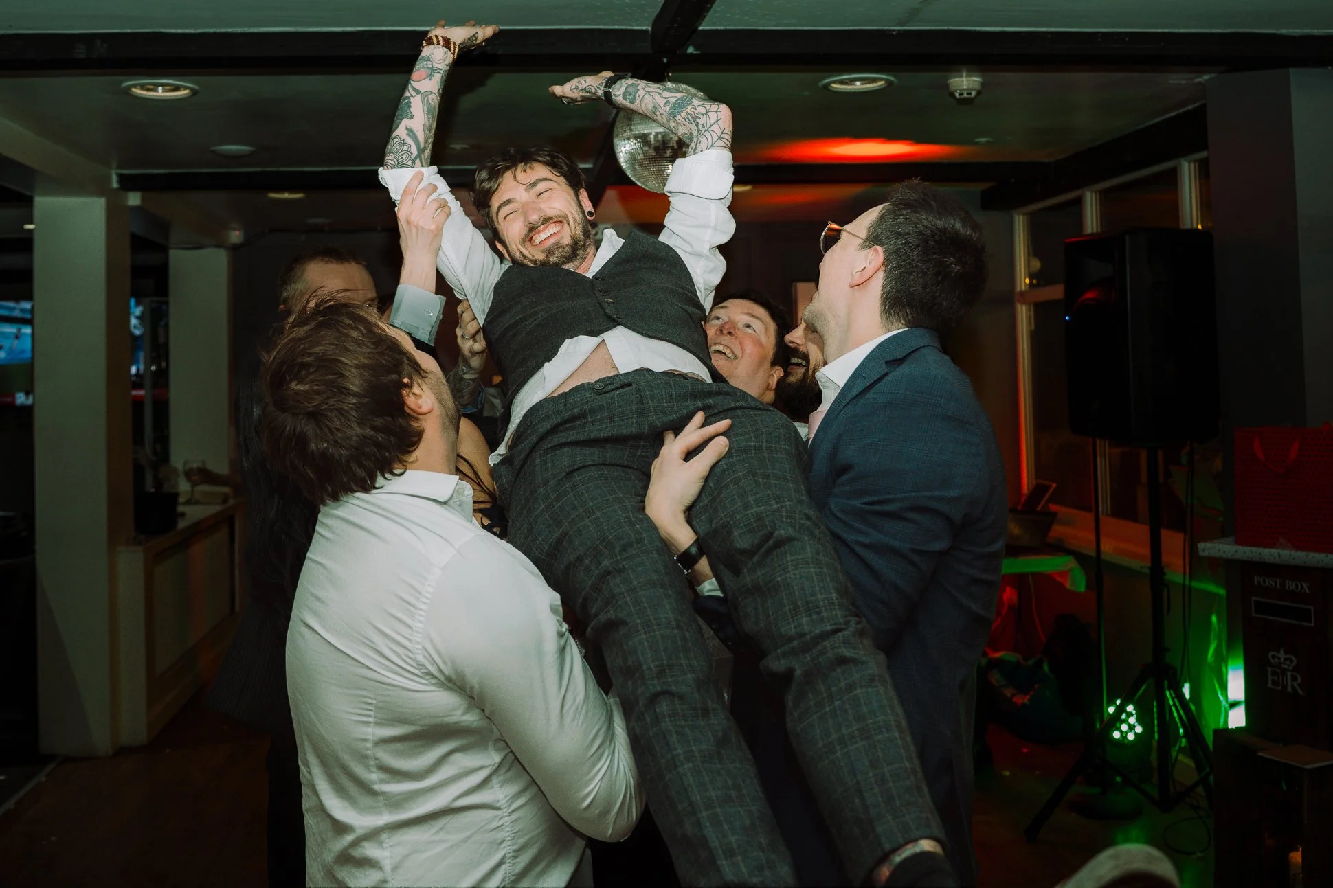 The tattooed groomsman has been fully lifted up until he is touching the ceiling and laughing