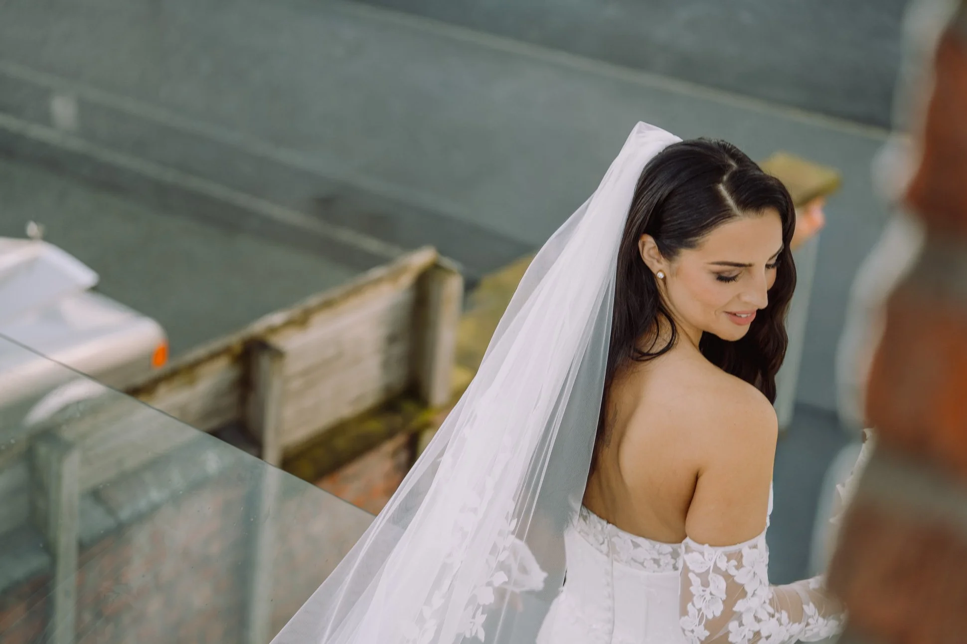 A candid image of a bride walking down some steps on the way to her wedding car. She is smiling and looking over her shoulder.