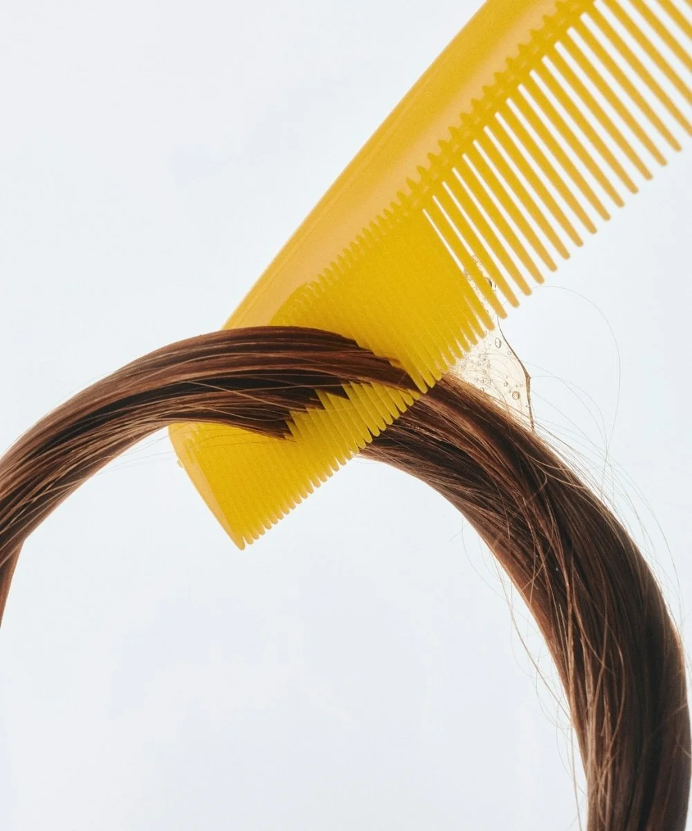 Close-up of a yellow hair comb detangling a strand of brown hair.