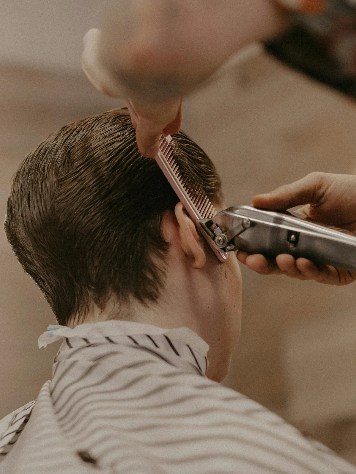 Barber trimming a man's hair with electric clippers in a barbershop.