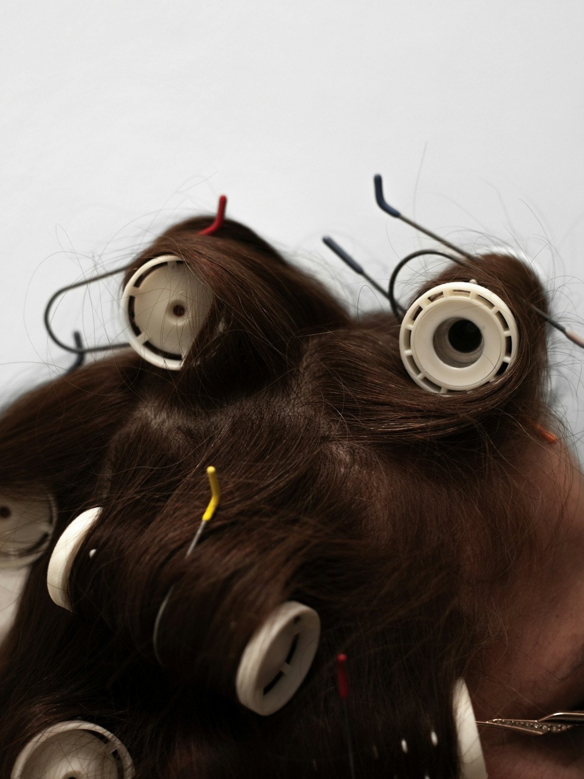 Hair rollers with brown hair wrapped around them, some with colorful pins, against a plain background.