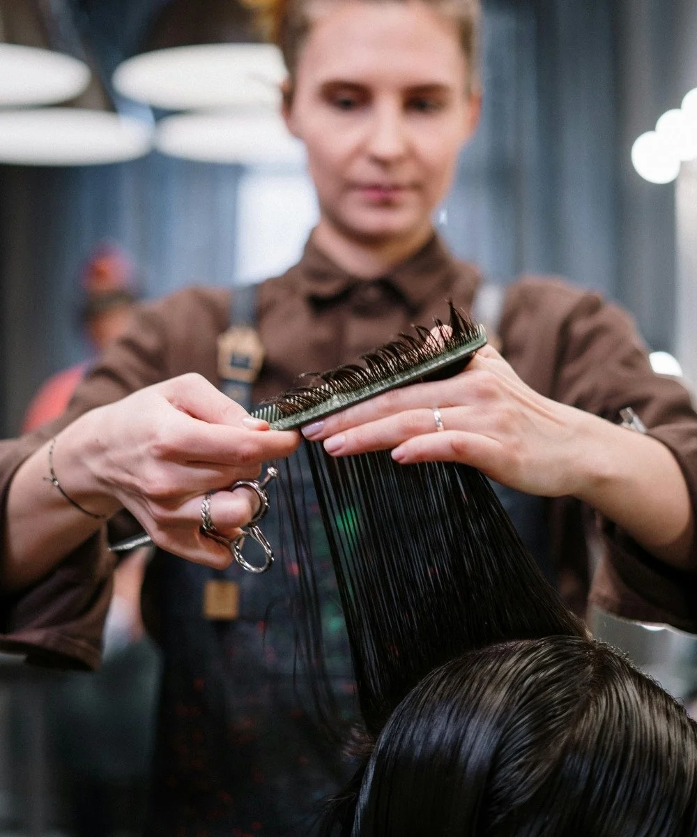 A hairdresser is dyeing a client's hair, holding a section of hair with a brush and a comb in a salon.