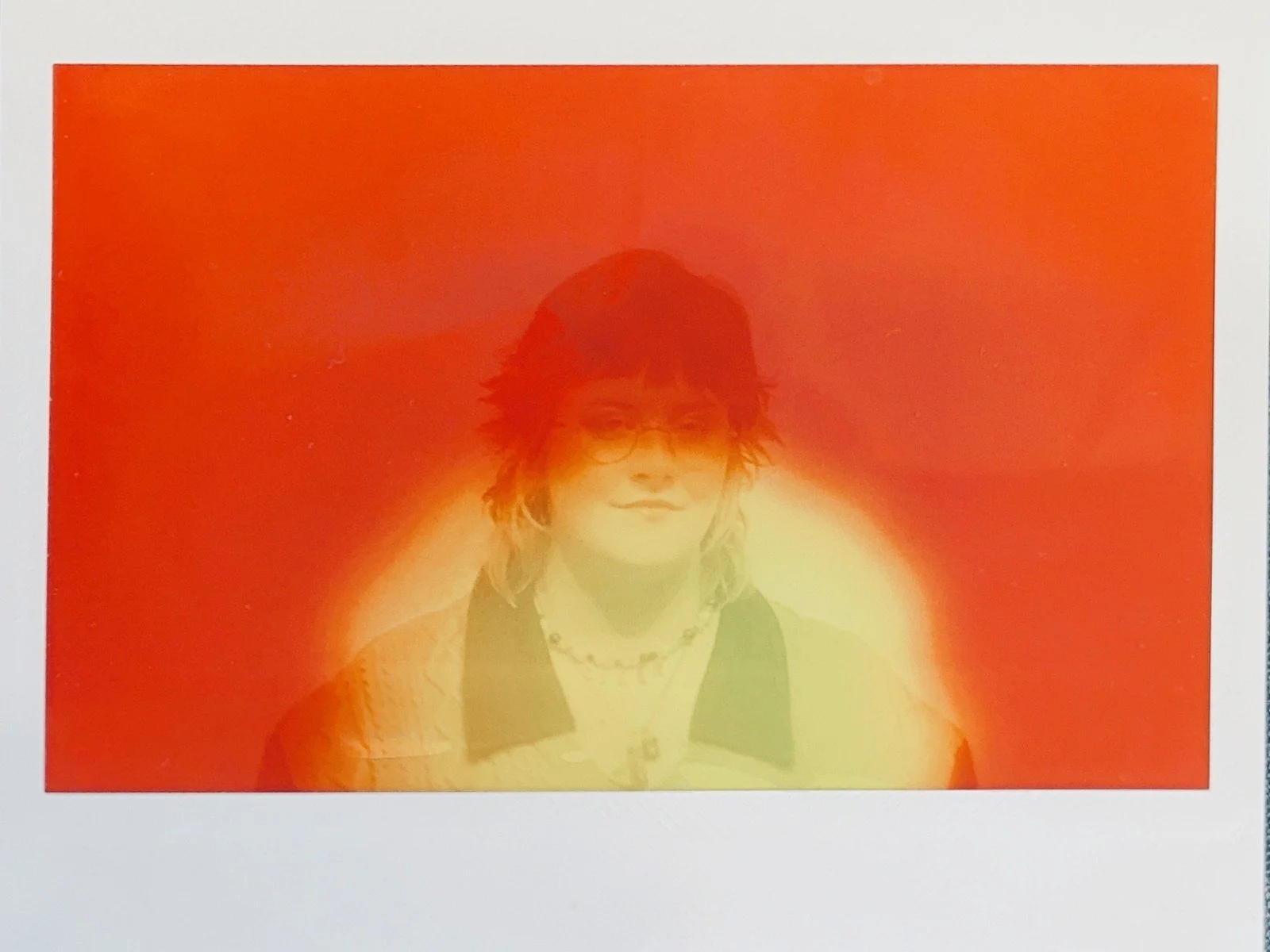 A person wearing glasses and a dark hat, smiling, with a brightly colored, glowing red and yellow background.