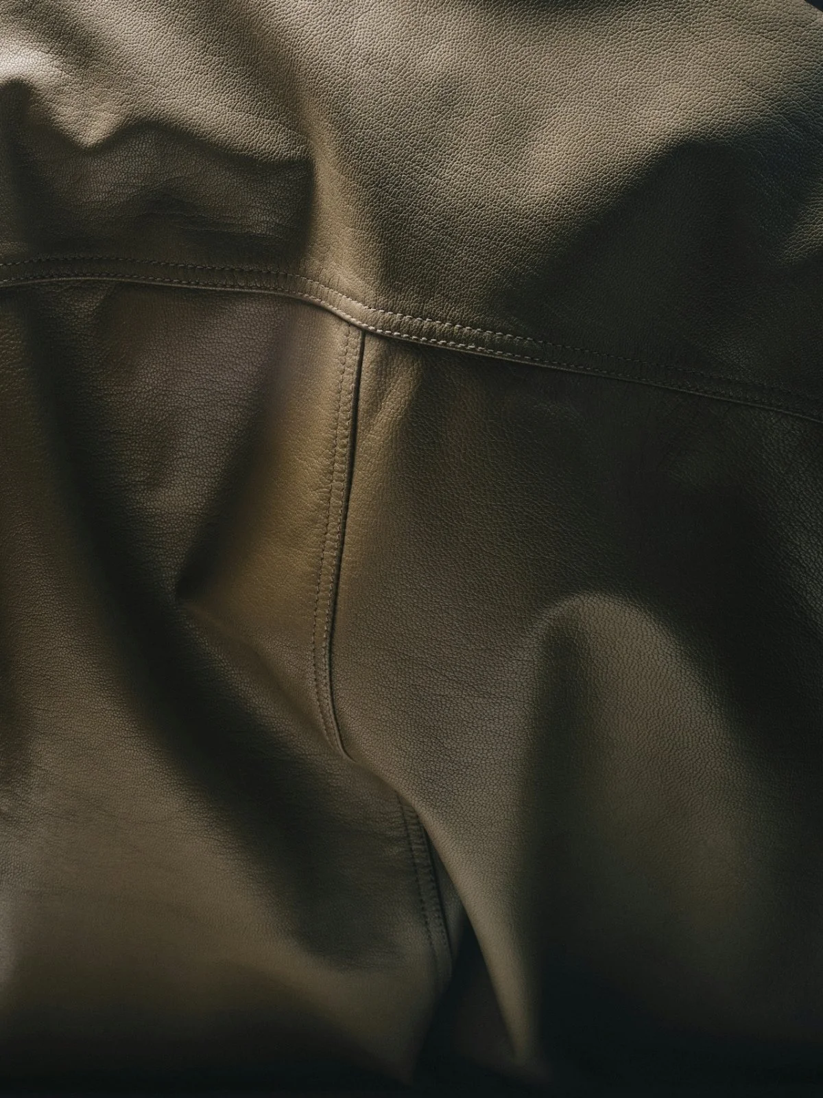 Close-up view of black leather fabric with visible stitching and textured surface.