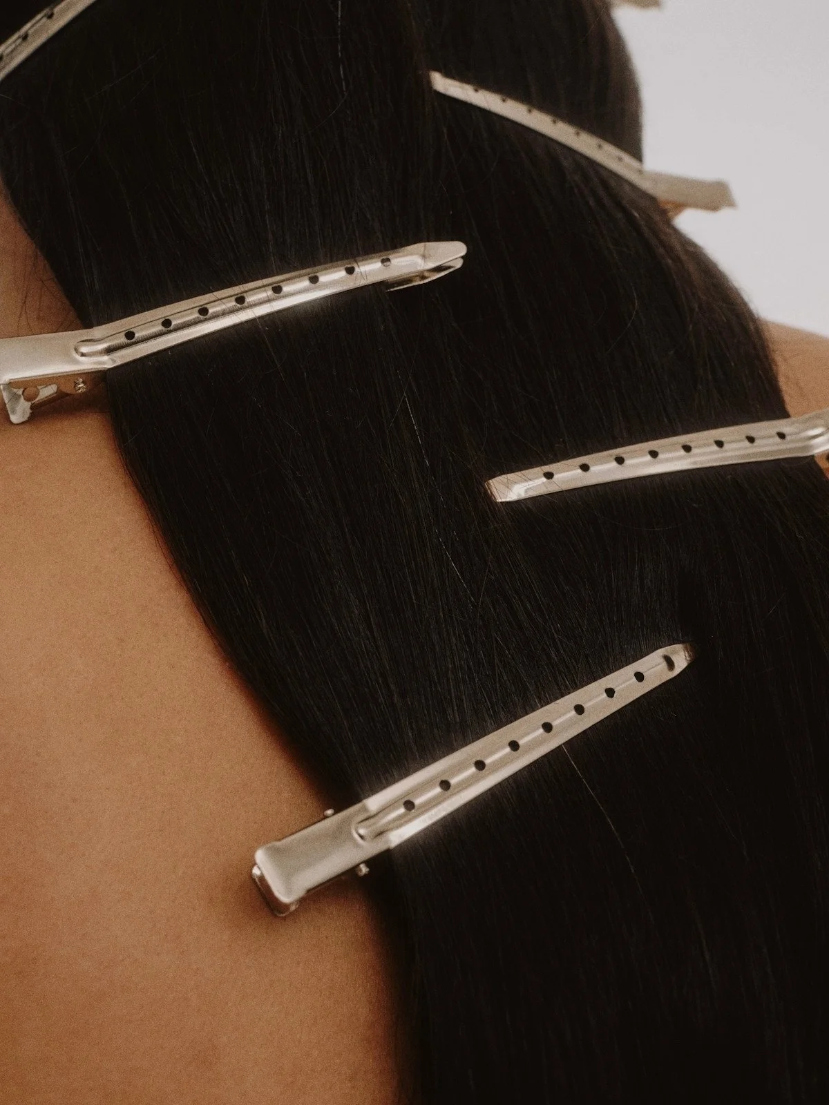Hair extensions with metal clips attached, secured to dark, straight hair.