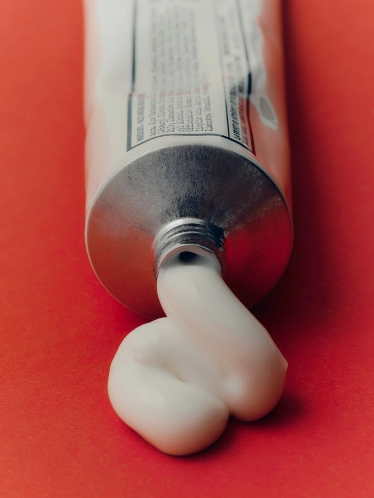 A tube with white toothpaste being squeezed out, placed on a red background.