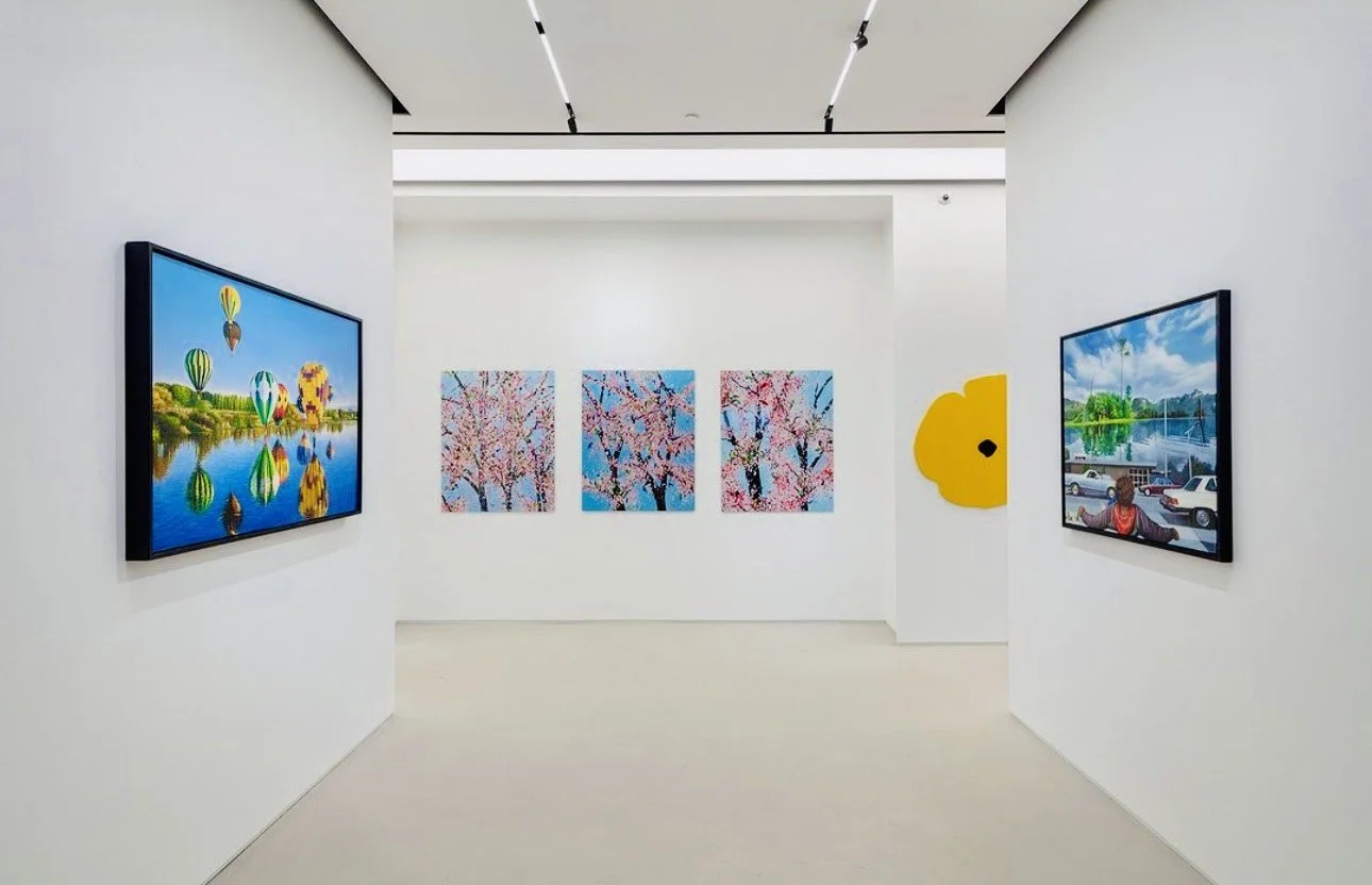 Art gallery with digital paintings, including hot air balloons over water, cherry blossom trees, and a scenic parking lot with a mural of a egg yolk on a white wall.
