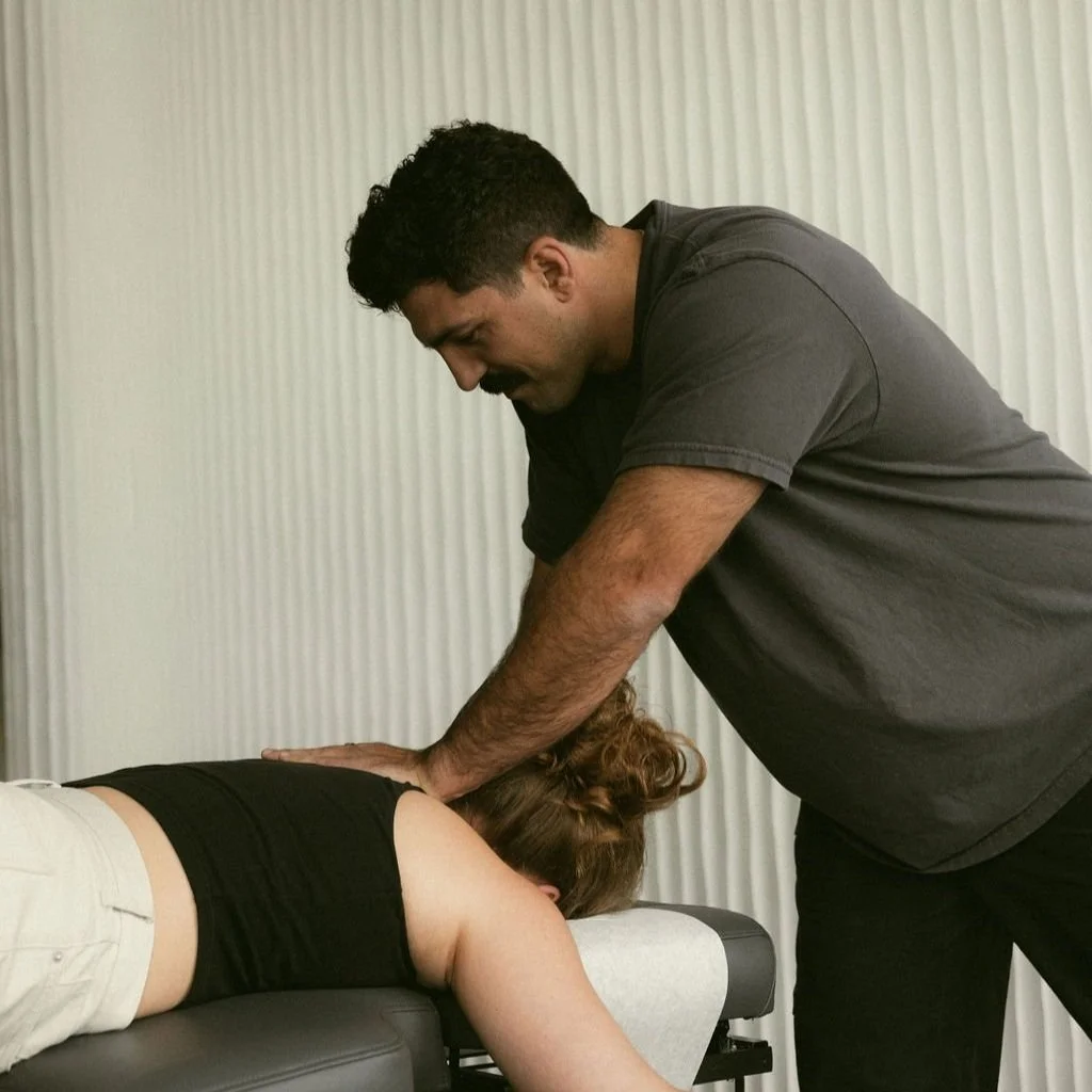 A man giving a chiropractic adjustment to a woman lying face down on a treatment table in a clinic setting.