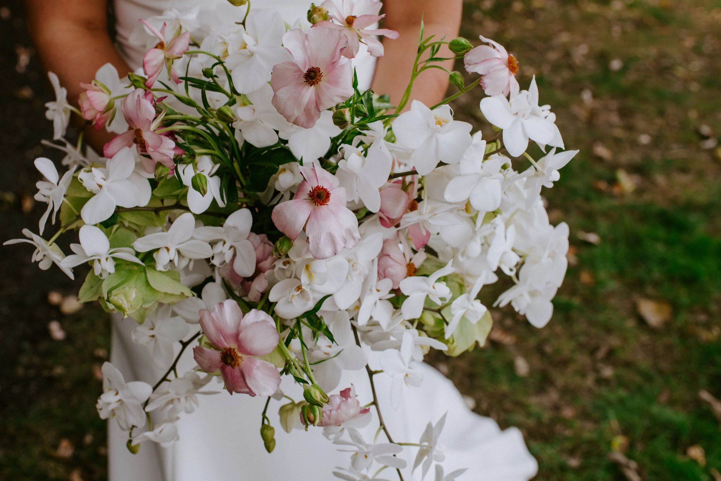 A person holding a large bouquet of white and light pink flowers outdoors with blurred ground in the background.