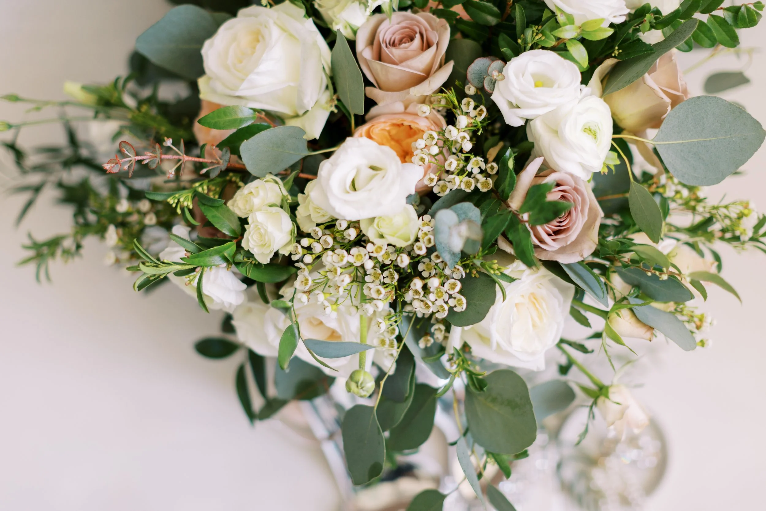 A close-up of a bouquet of white, cream, and blush roses with assorted green foliage and small white filler flowers.
