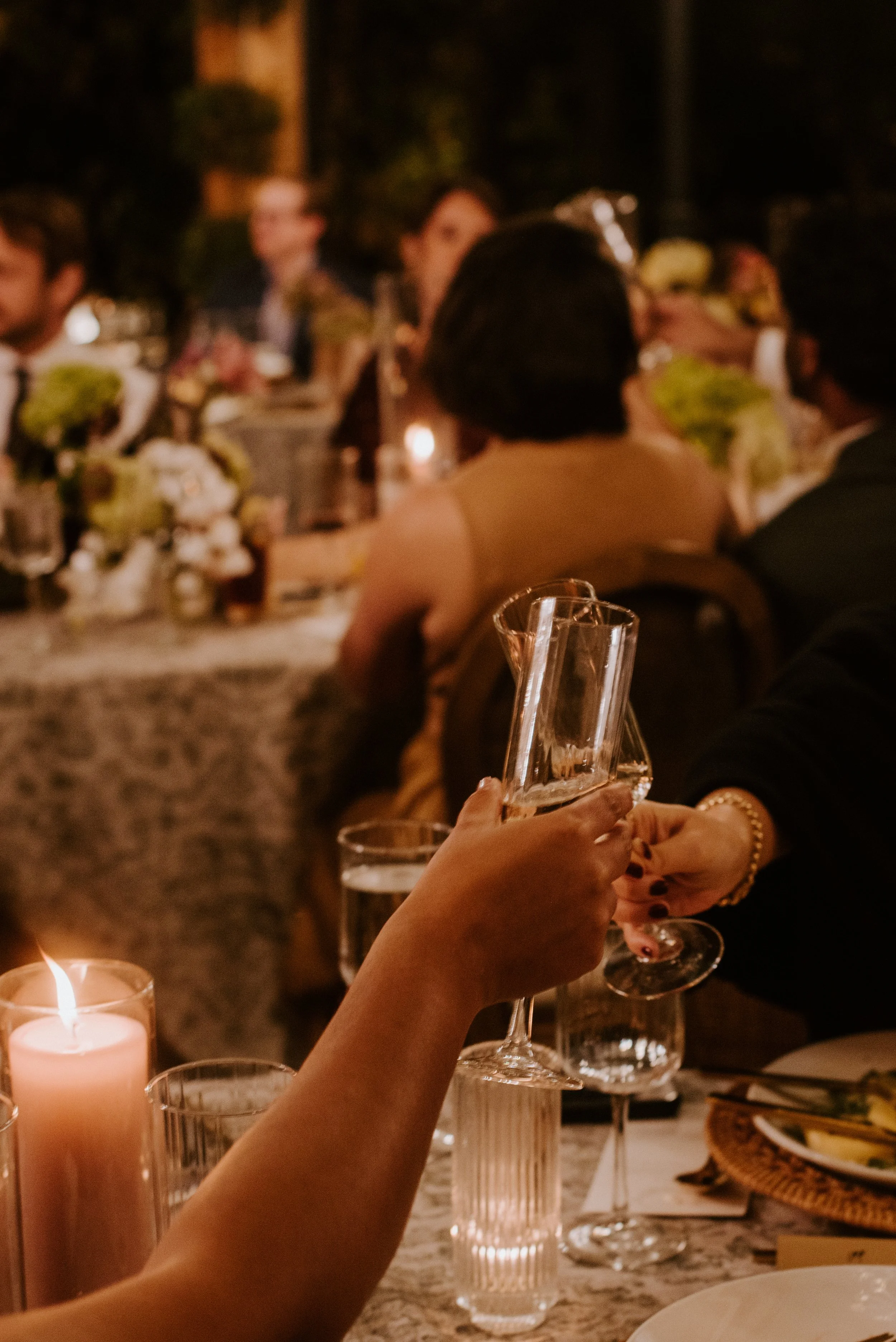A person holding a champagne glass at dinner with candles and a festive table setting, celebrating at night.