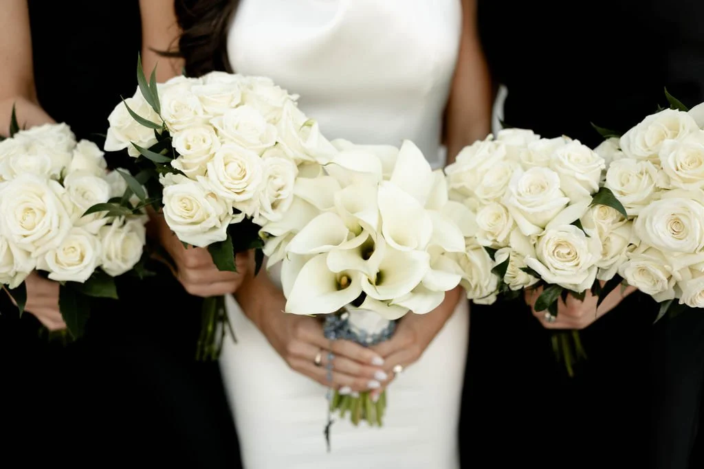 A bride holding a bouquet of white calla lilies, surrounded by people holding white roses