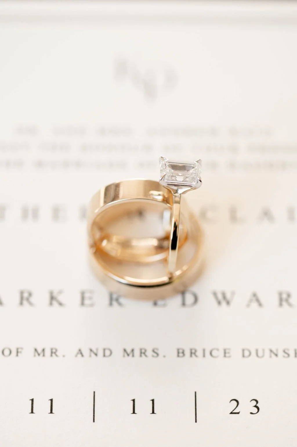 Close-up of two wedding rings, one with a square-cut diamond, placed on a wedding program.