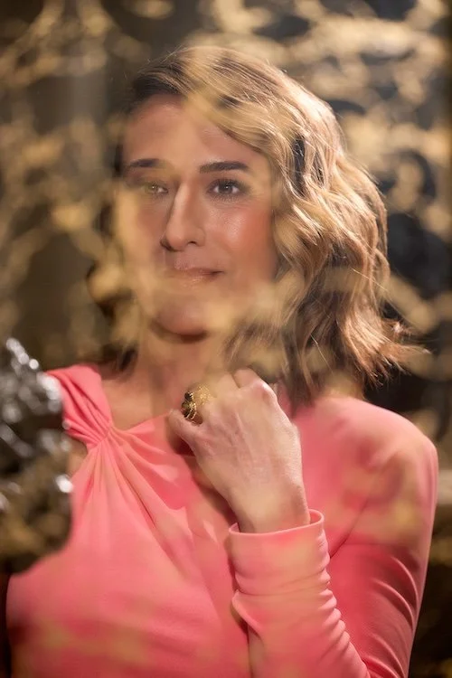 Woman in a vibrant pink top with a confident, reflective expression against a warm, blurred background—embodying empowerment and self-assurance.