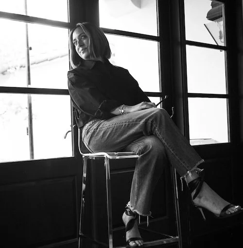 Woman sitting on a bar stool by large industrial windows in black and white photograph