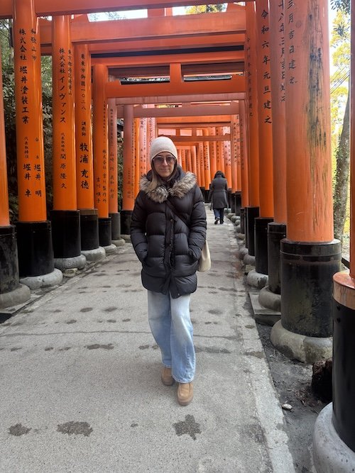 Woman walking through orange torii gate tunnel at Fushimi Inari Shrine in Kyoto, Japan