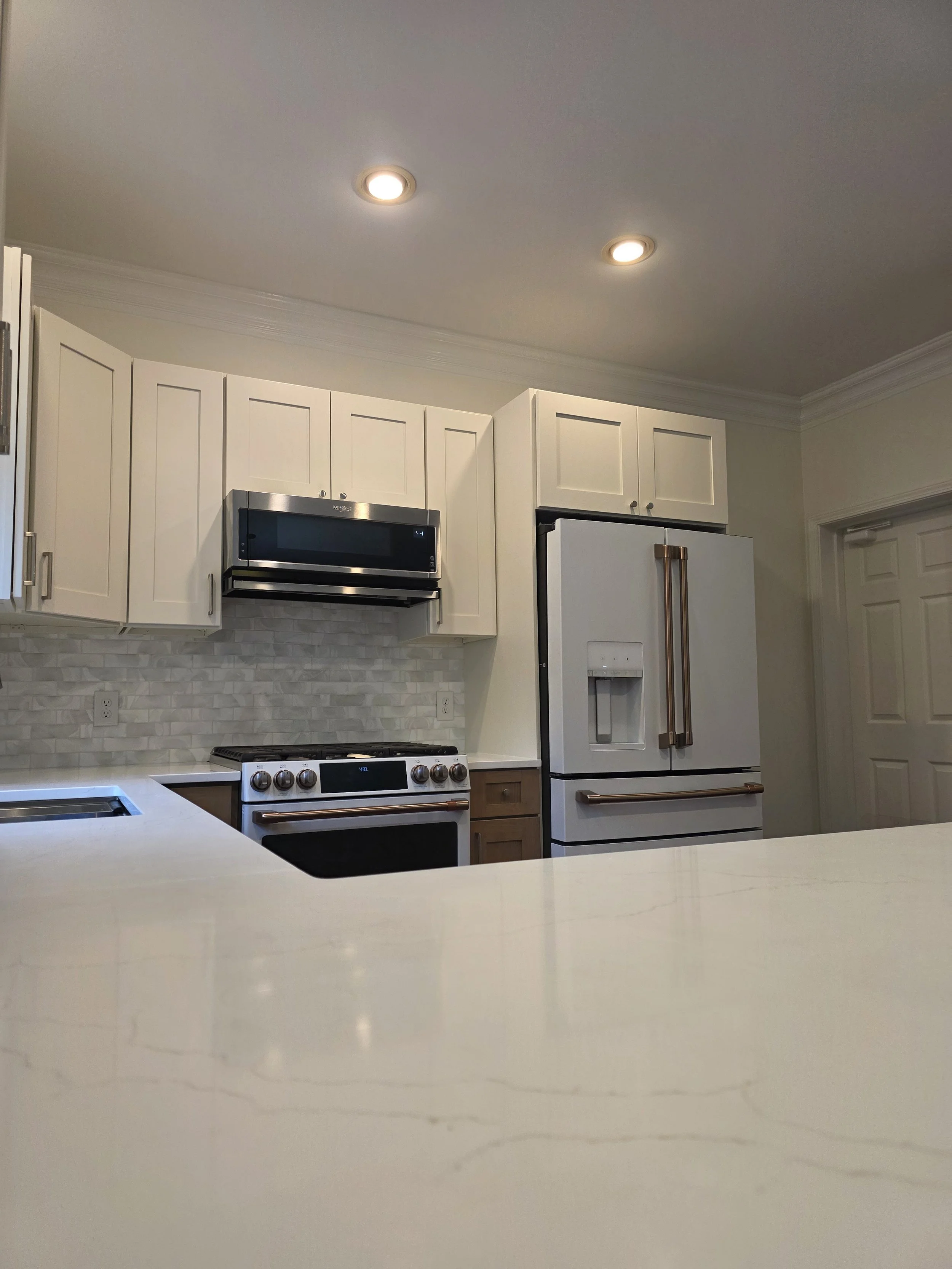 View across the kitchen peninsula toward the range, refrigerator, and white upper cabinets.