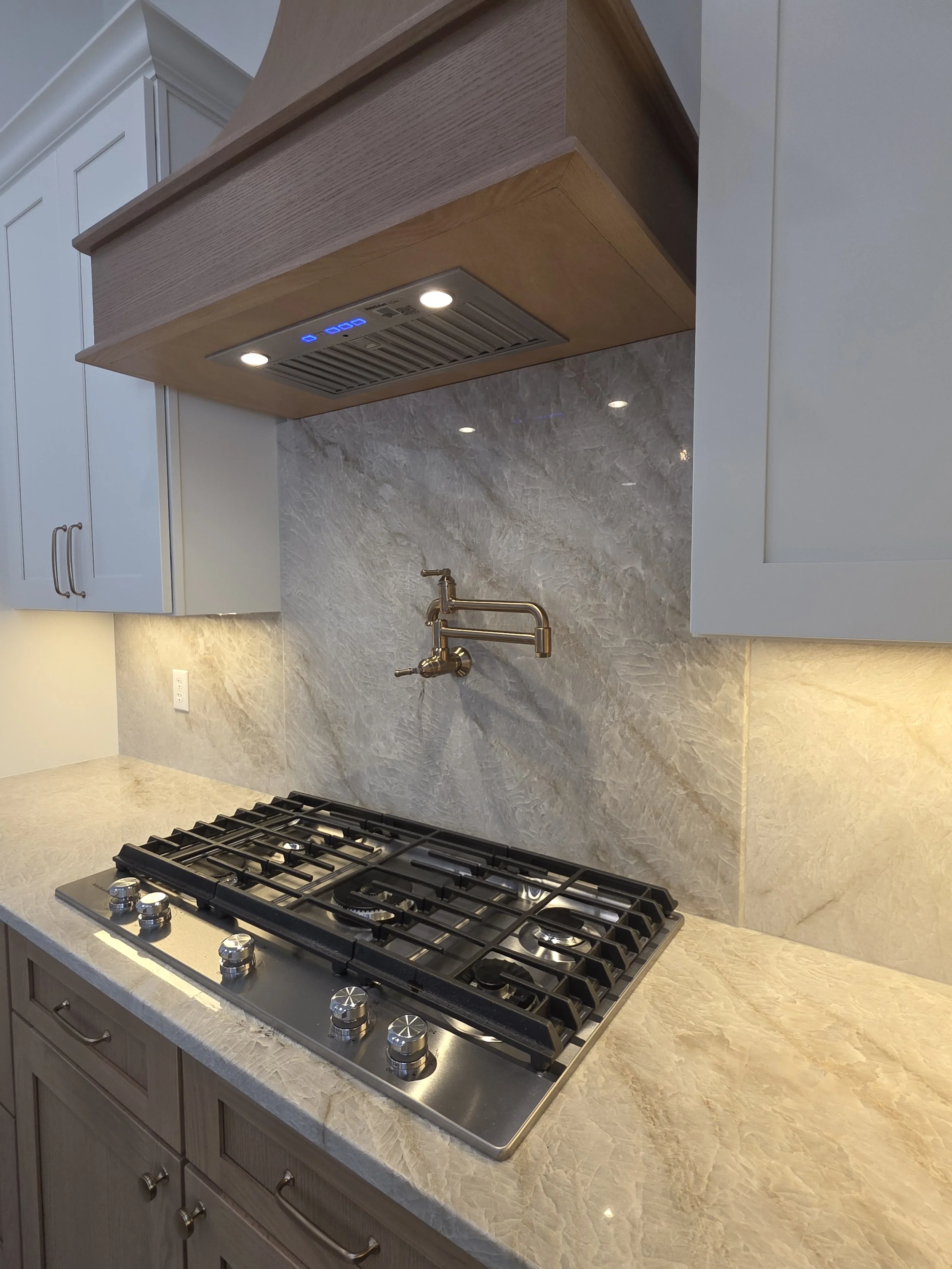 Close view of the cooktop, pot filler and illuminated range hood.