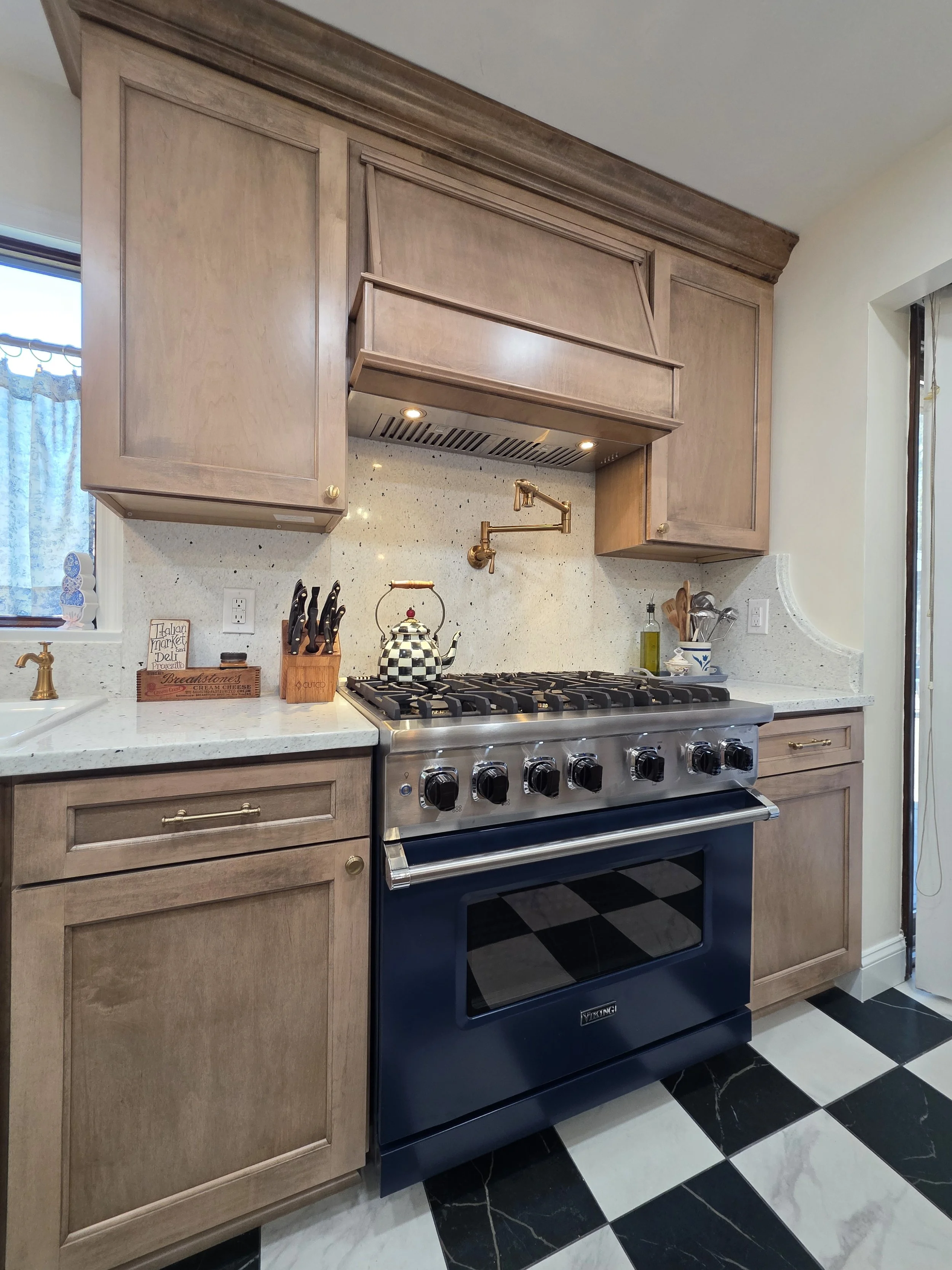 Close view of the decorative wood range hood, dark range and gold-tone pot filler.