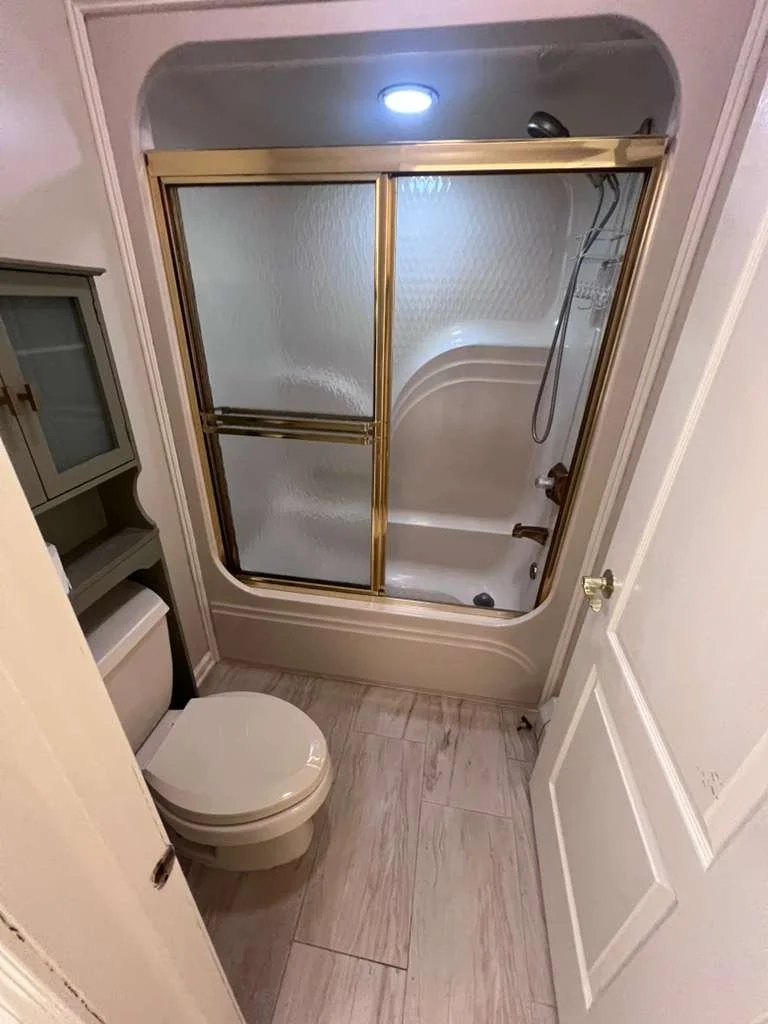 Before renovation: the original tub and framed sliding shower doors beside the toilet.