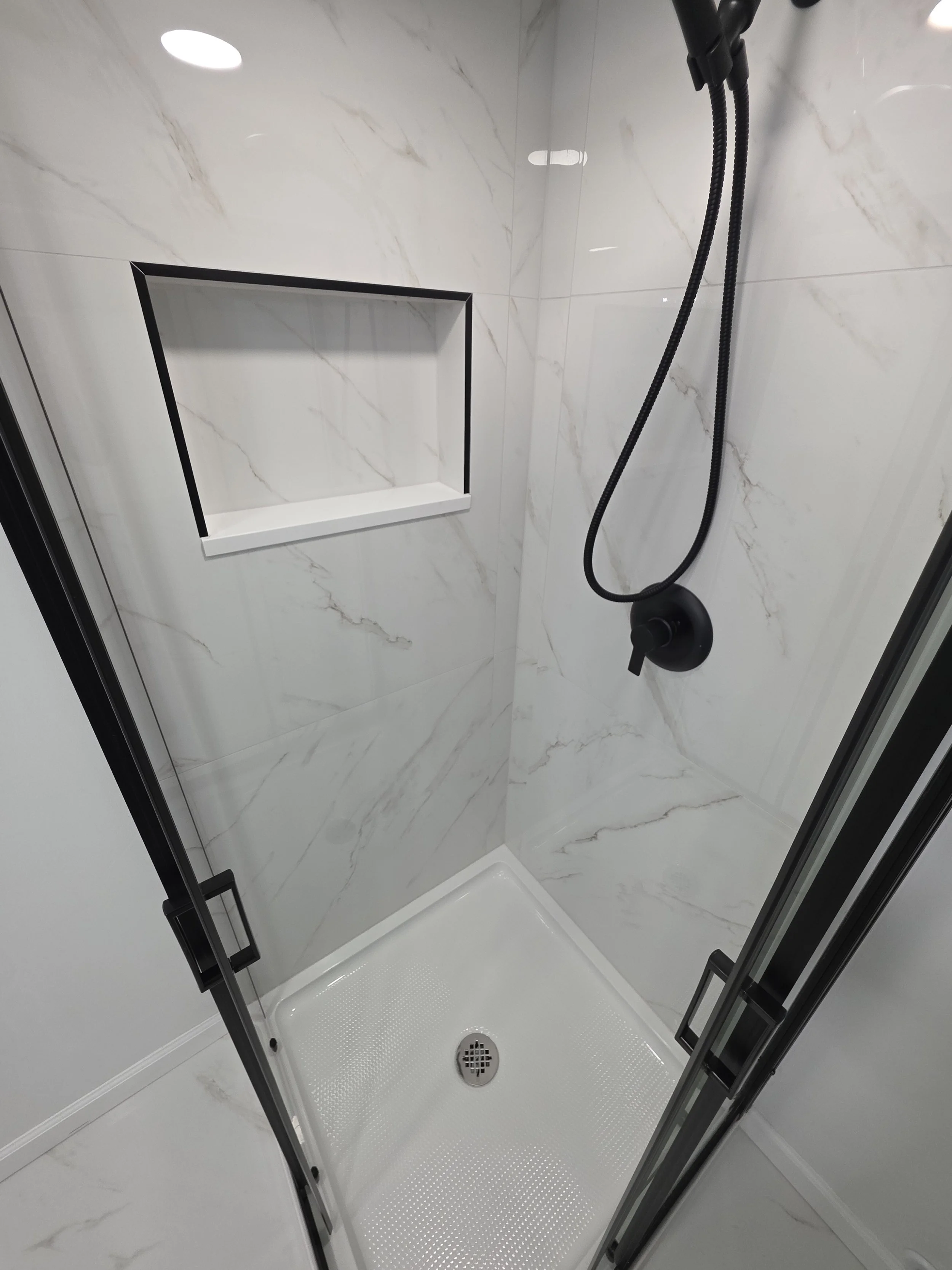 Shower floor and recessed niche inside the black-framed corner enclosure.