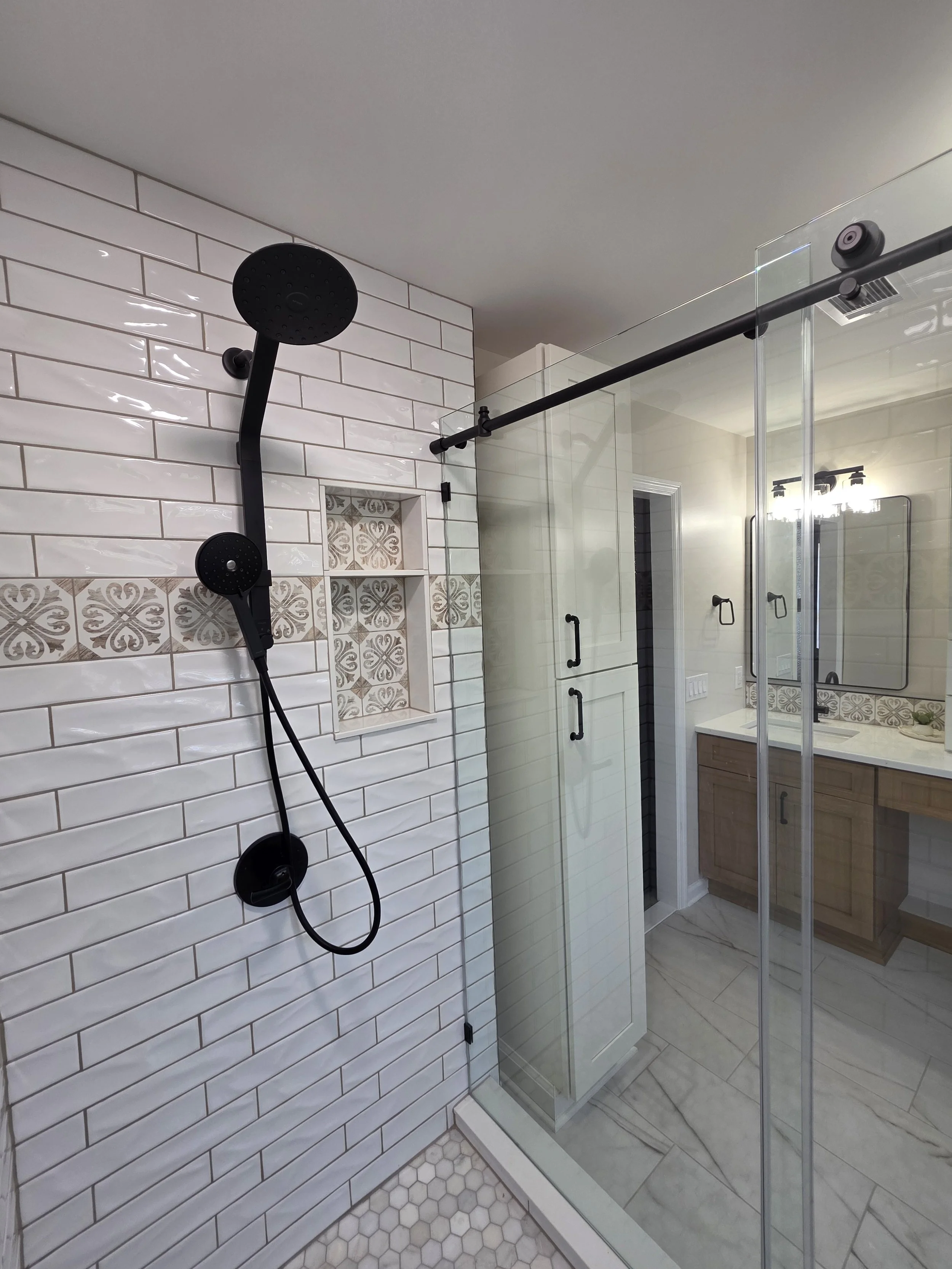 Black handheld shower and glass enclosure beside white subway tile with a patterned accent band.
