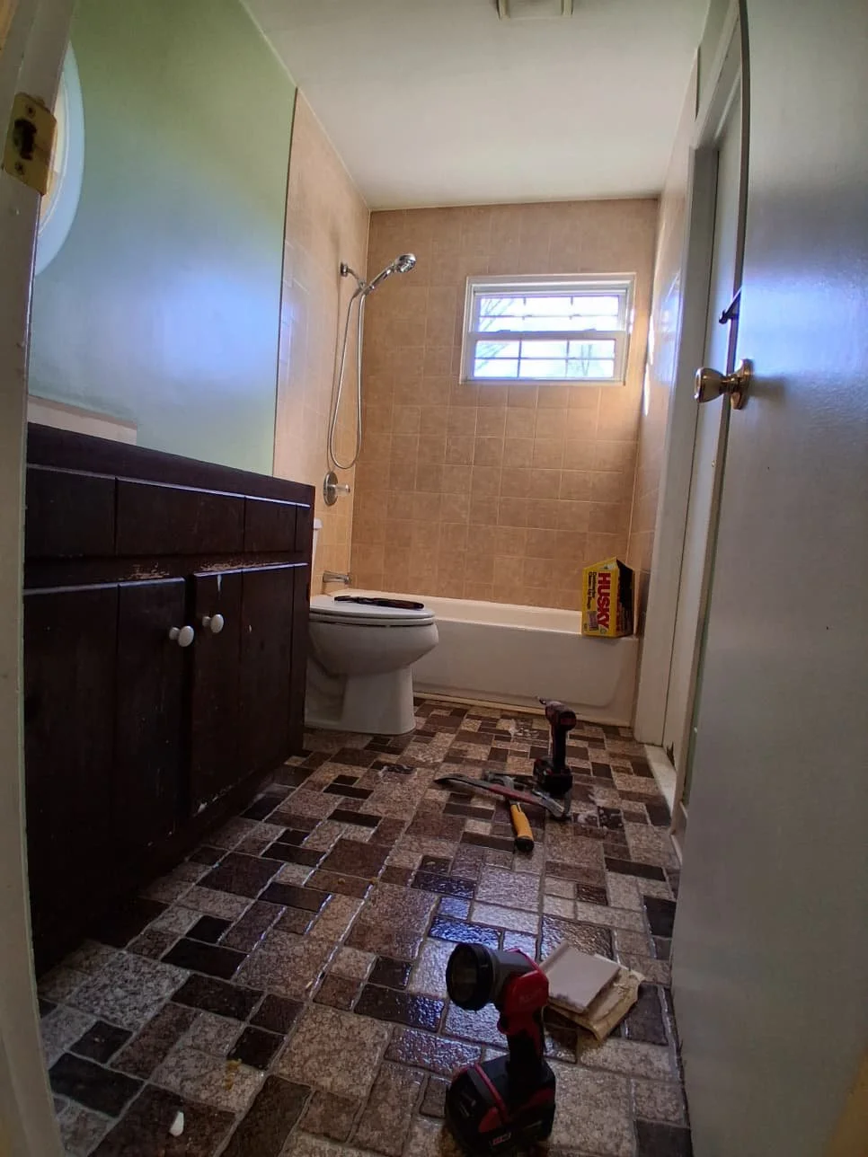 Before renovation: the original hallway bathroom with a dark vanity, patterned floor and older tub surround.