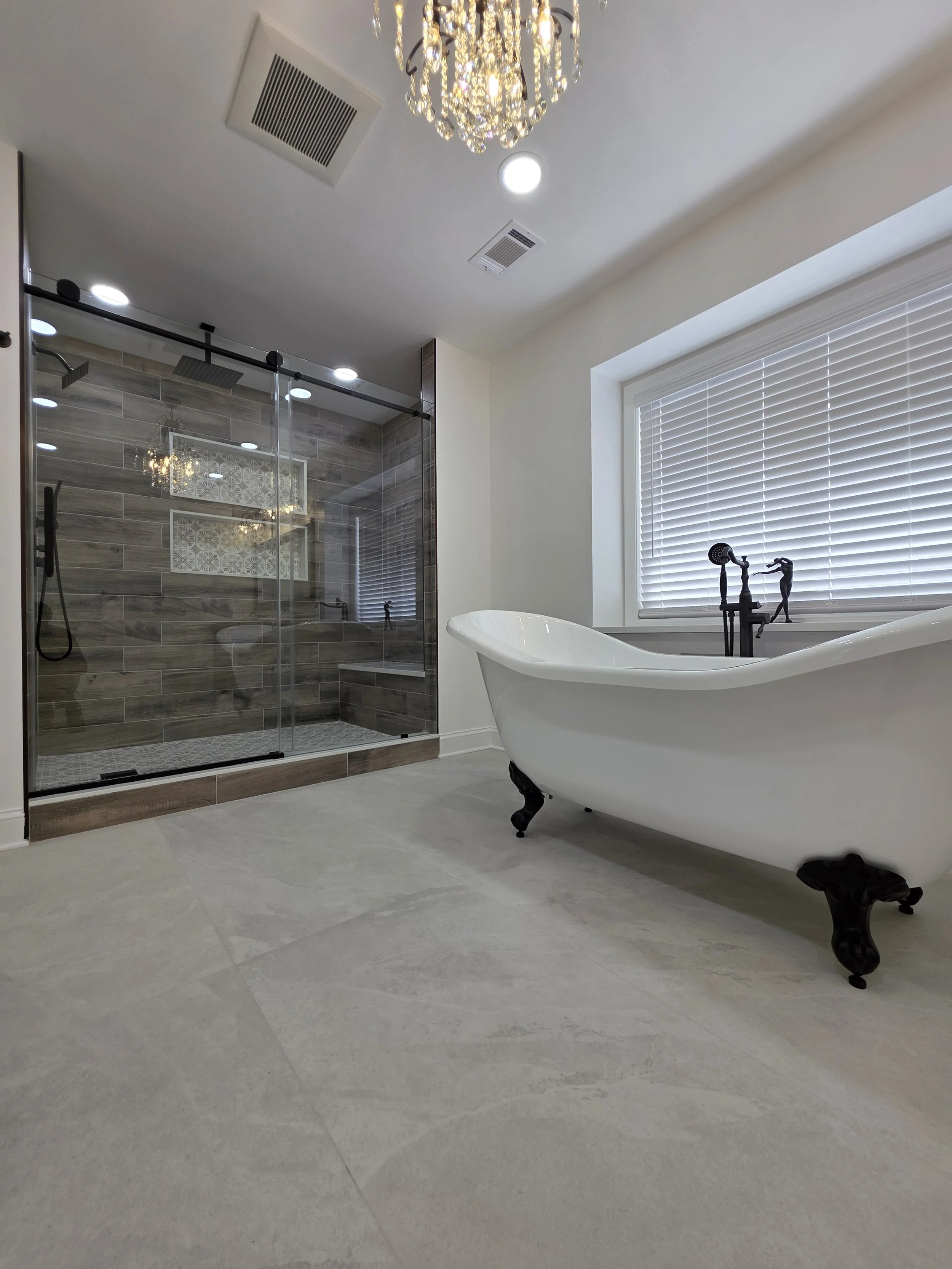 Lucy and John’s remodeled master bathroom with a clawfoot tub, chandelier and glass shower with wood-look tile.