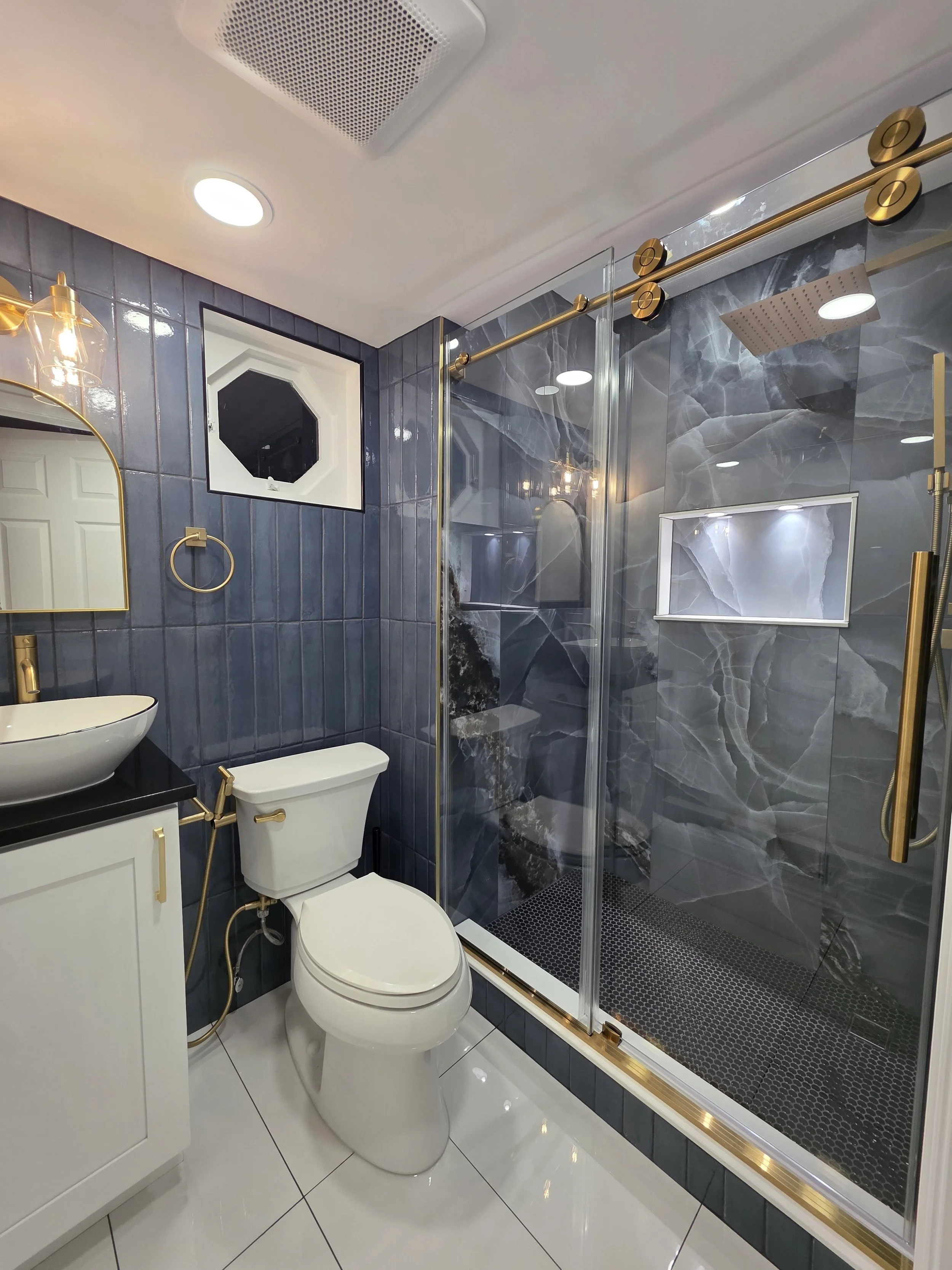 Omar’s remodeled first-floor bathroom with a glass shower, dramatic veined tile, gold-tone hardware and vessel-sink vanity.