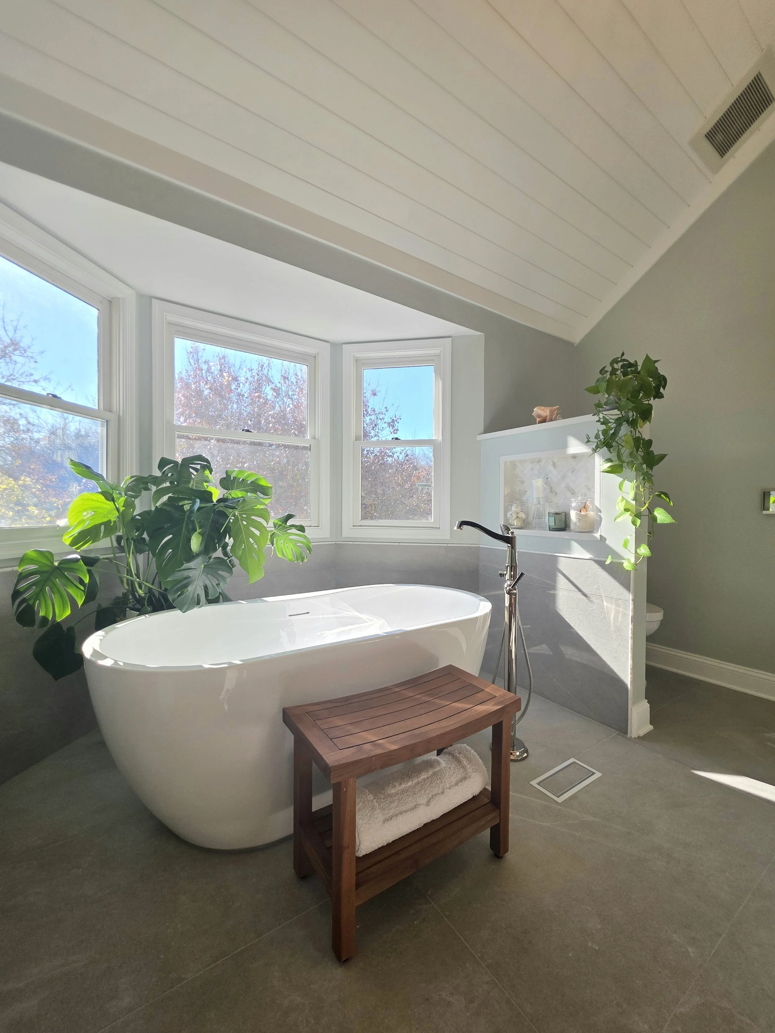 Luxury organic modern master bathroom with freestanding soaking tub, vaulted shiplap ceiling, large windows, soft sage walls, gray porcelain tile flooring, and spa-inspired natural wood accents in Central NJ remodel.