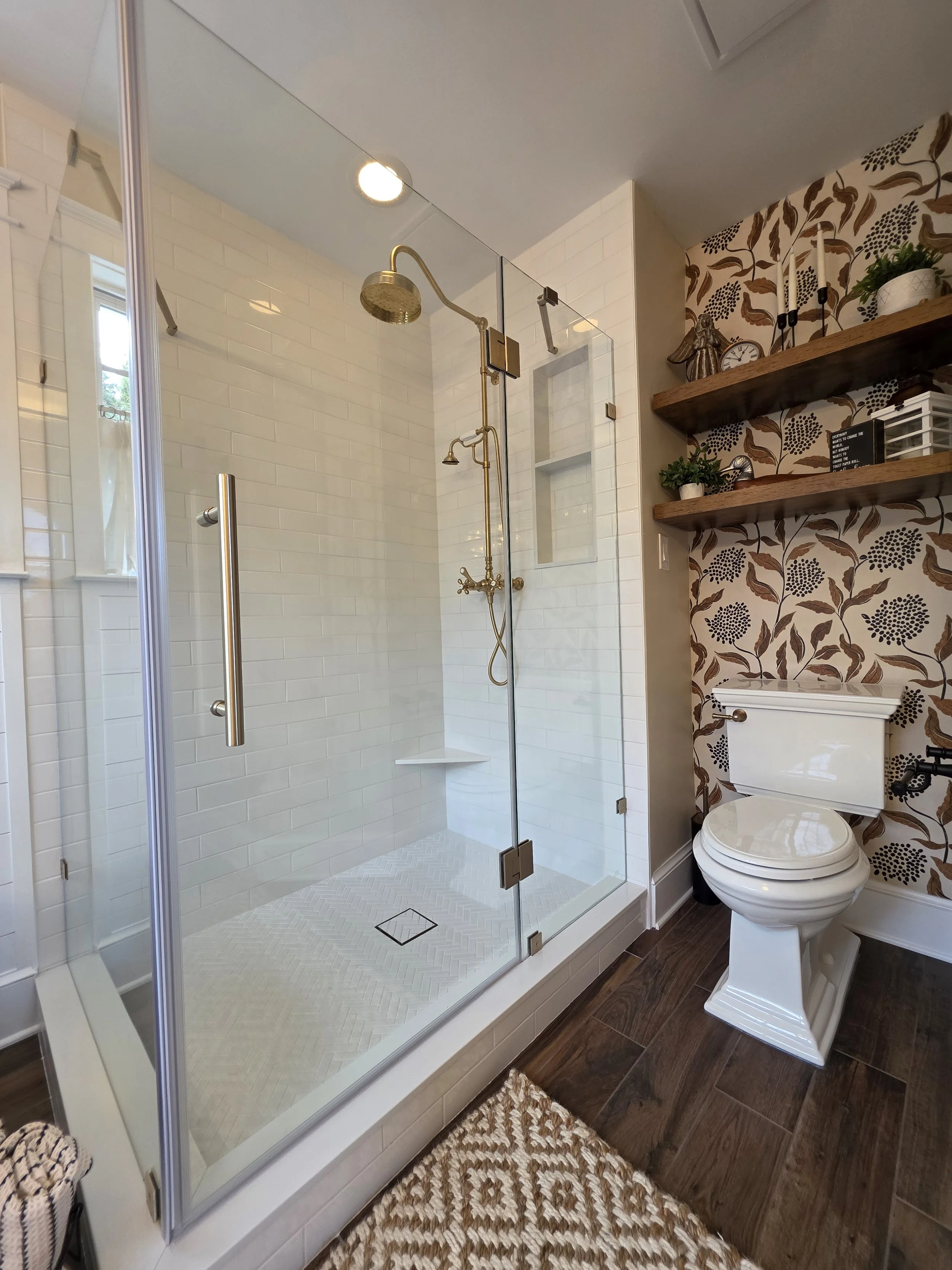 Glass shower beside decorative wallpaper and open shelving.