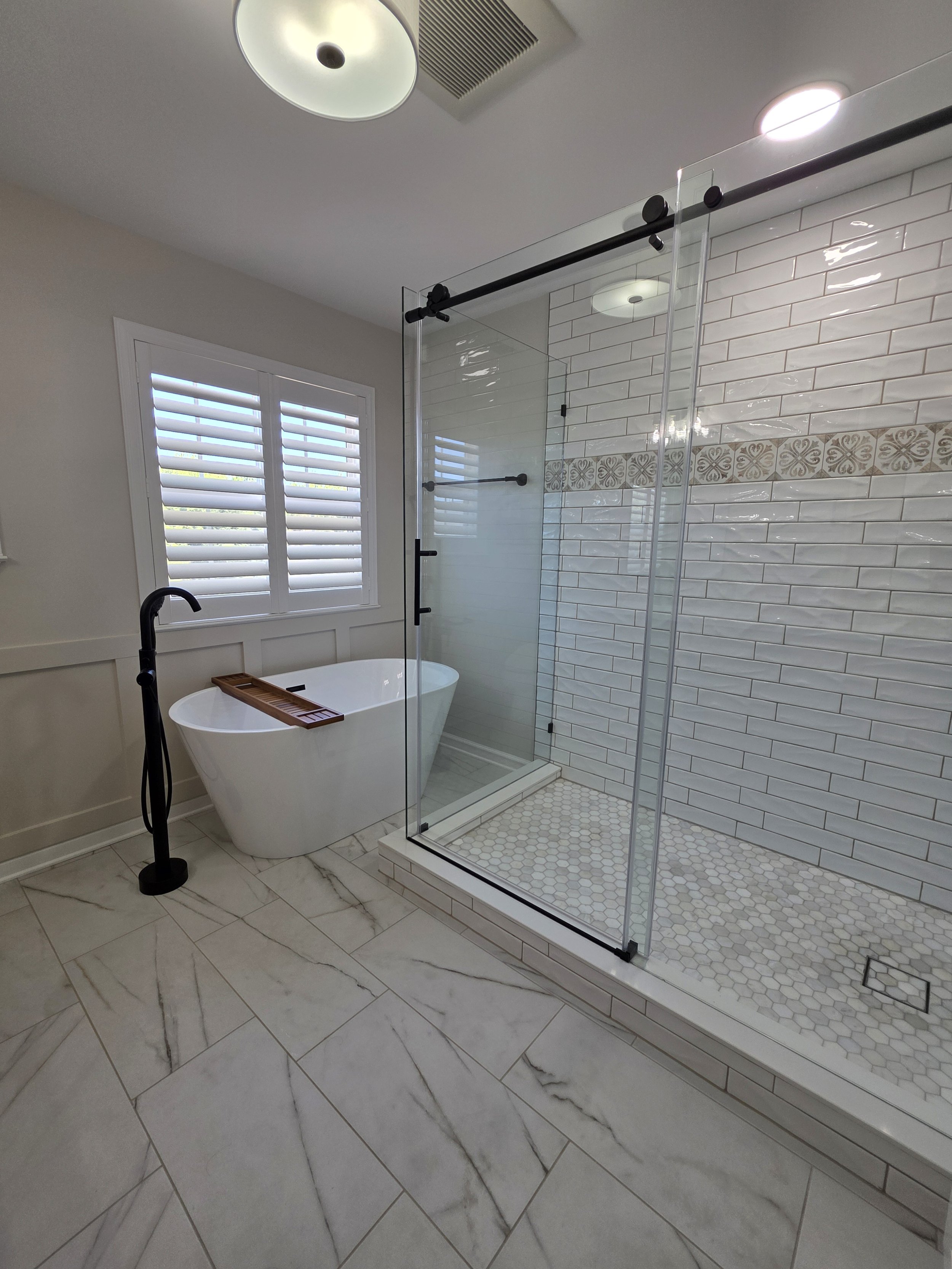 Freestanding bathtub beside the glass shower enclosure with black sliding-door hardware.