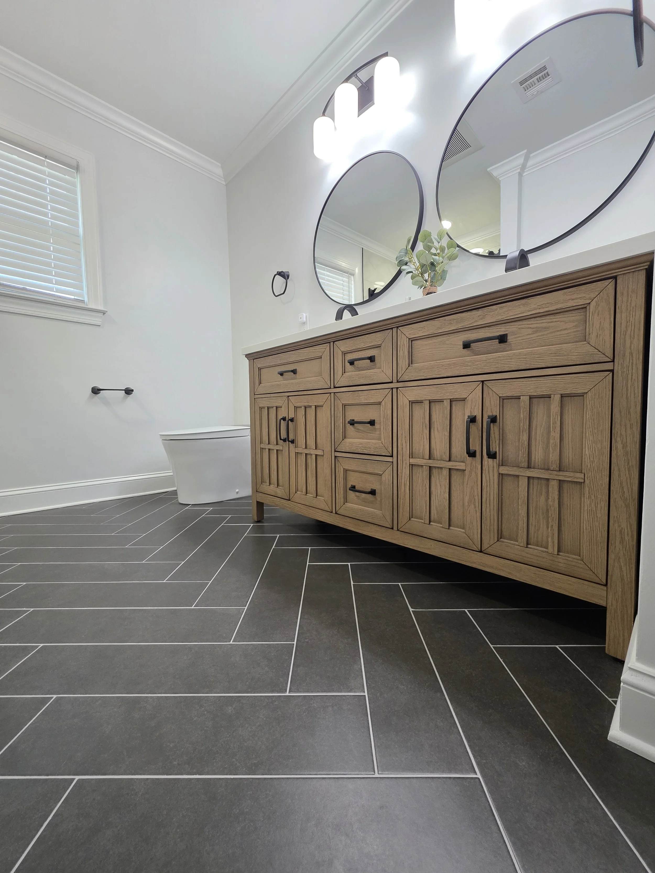 Low view of the wood-tone vanity cabinetry and dark herringbone floor tile.