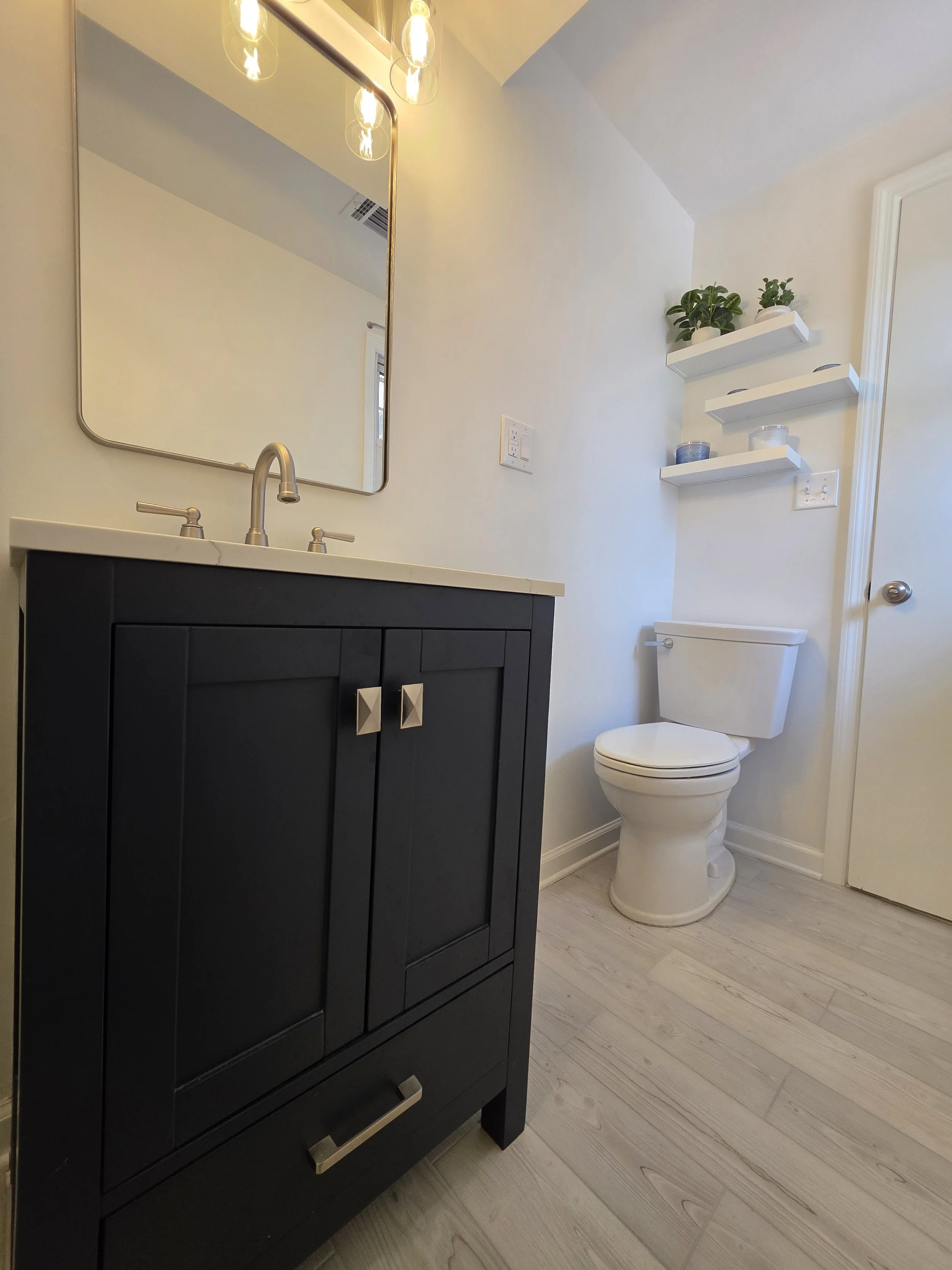 Low view of the navy vanity, light countertop and toilet beside the bathroom door.