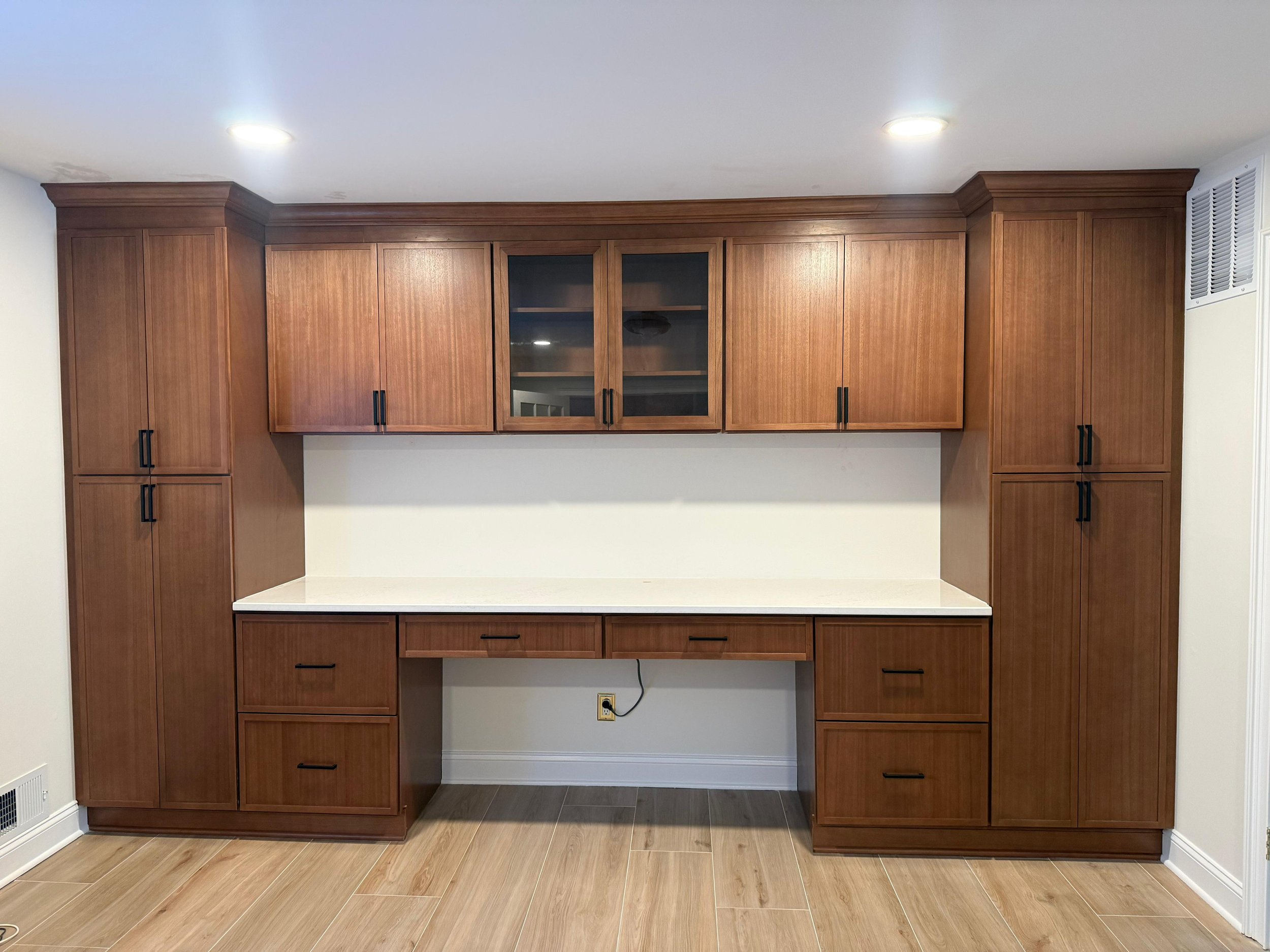 Vincent and Angela’s office built-ins with wood cabinets, glass-front upper doors and an integrated light-colored desktop.