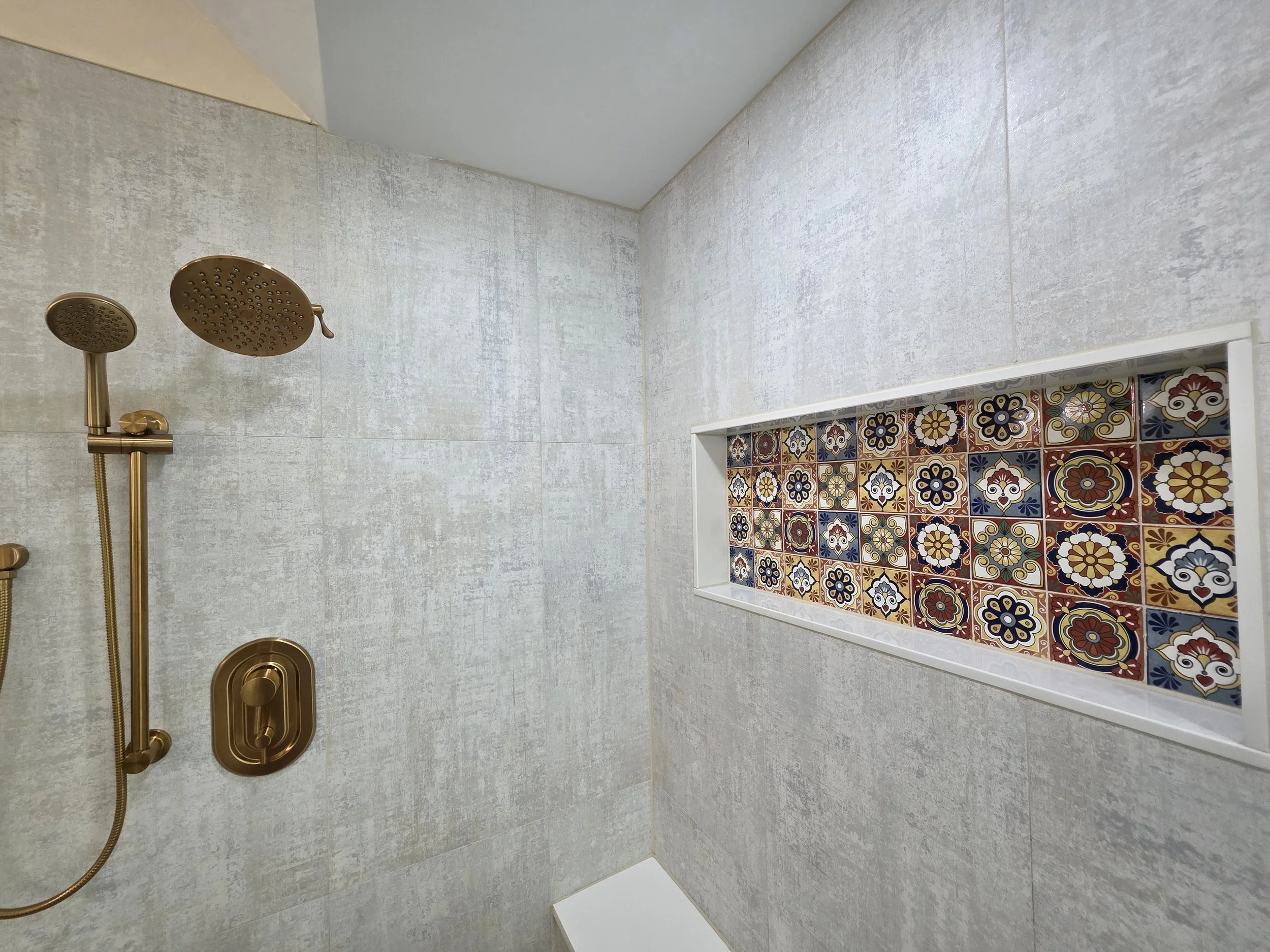 Close view of gold-tone shower fixtures and the long patterned recessed niche.