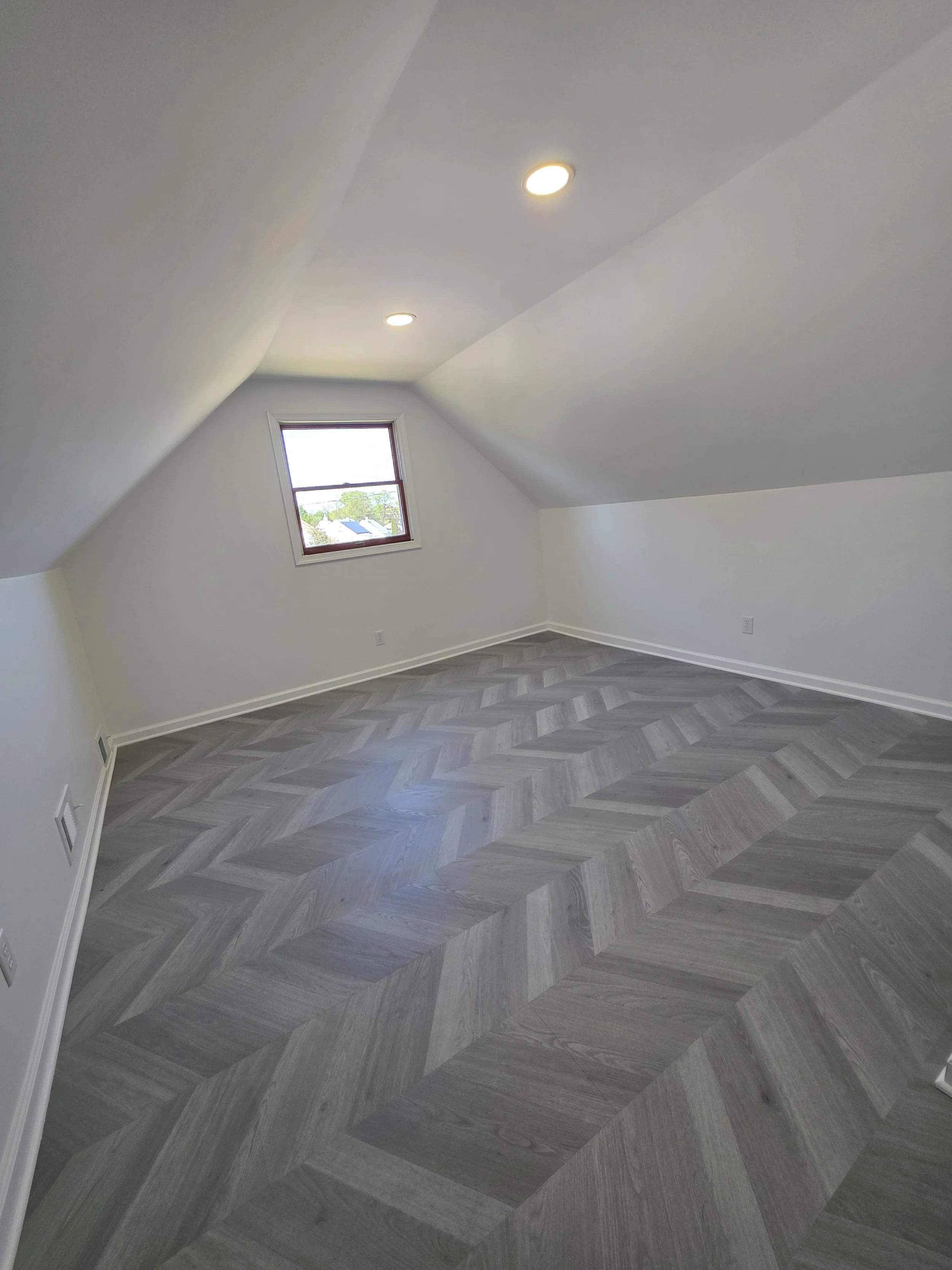 Refreshed upstairs room beneath a sloped ceiling with a single window.