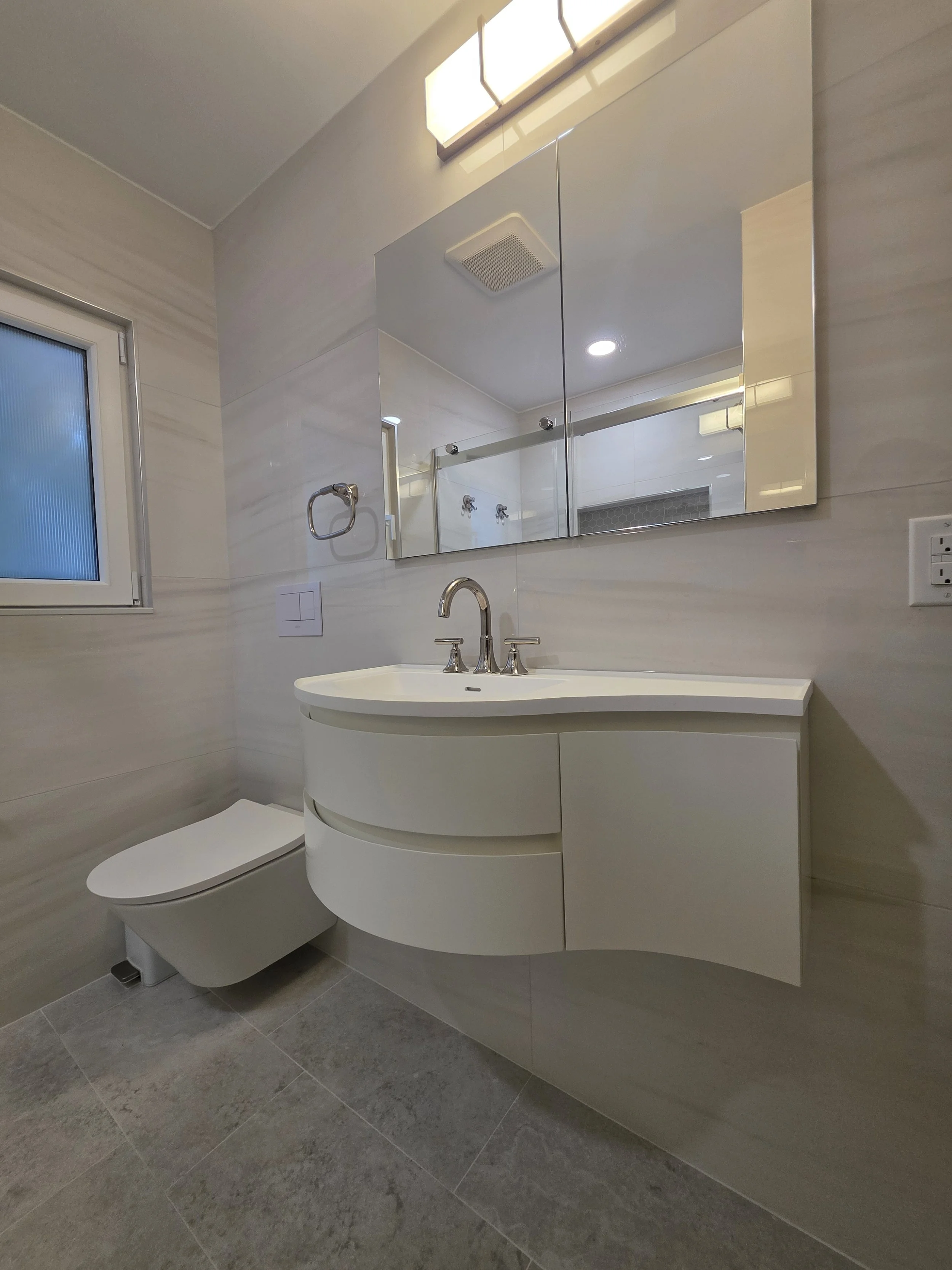 Curved white floating vanity beside wall-hung toilet.