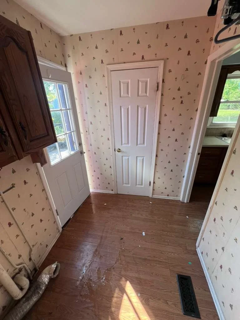 Before renovation: laundry-room entry with wallpaper and the original floor.