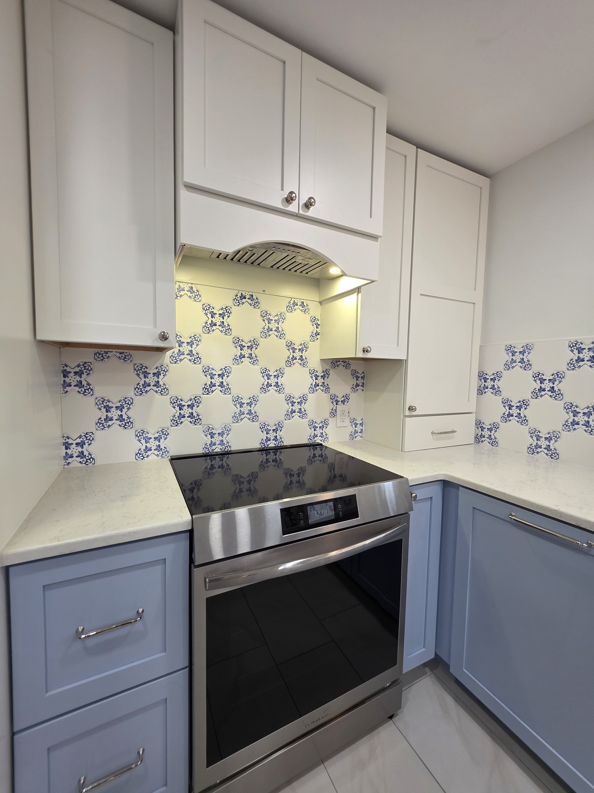 White upper cabinets and patterned tile above the range.