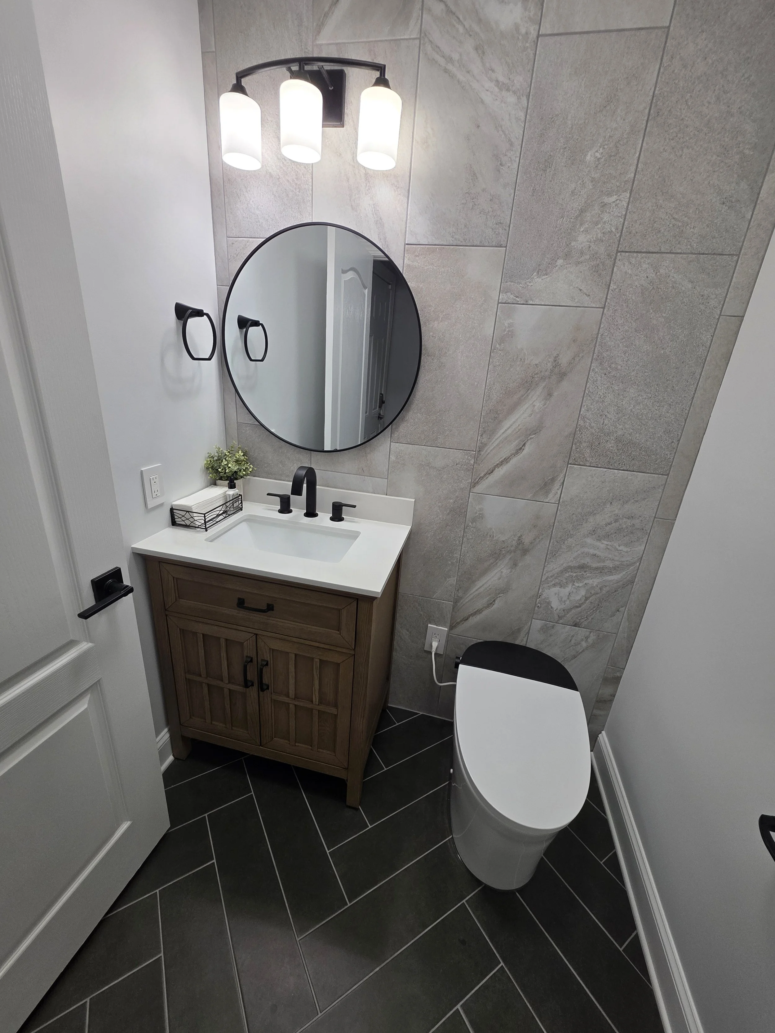 Wide view from the powder-room doorway showing the vanity, round mirror and toilet.
