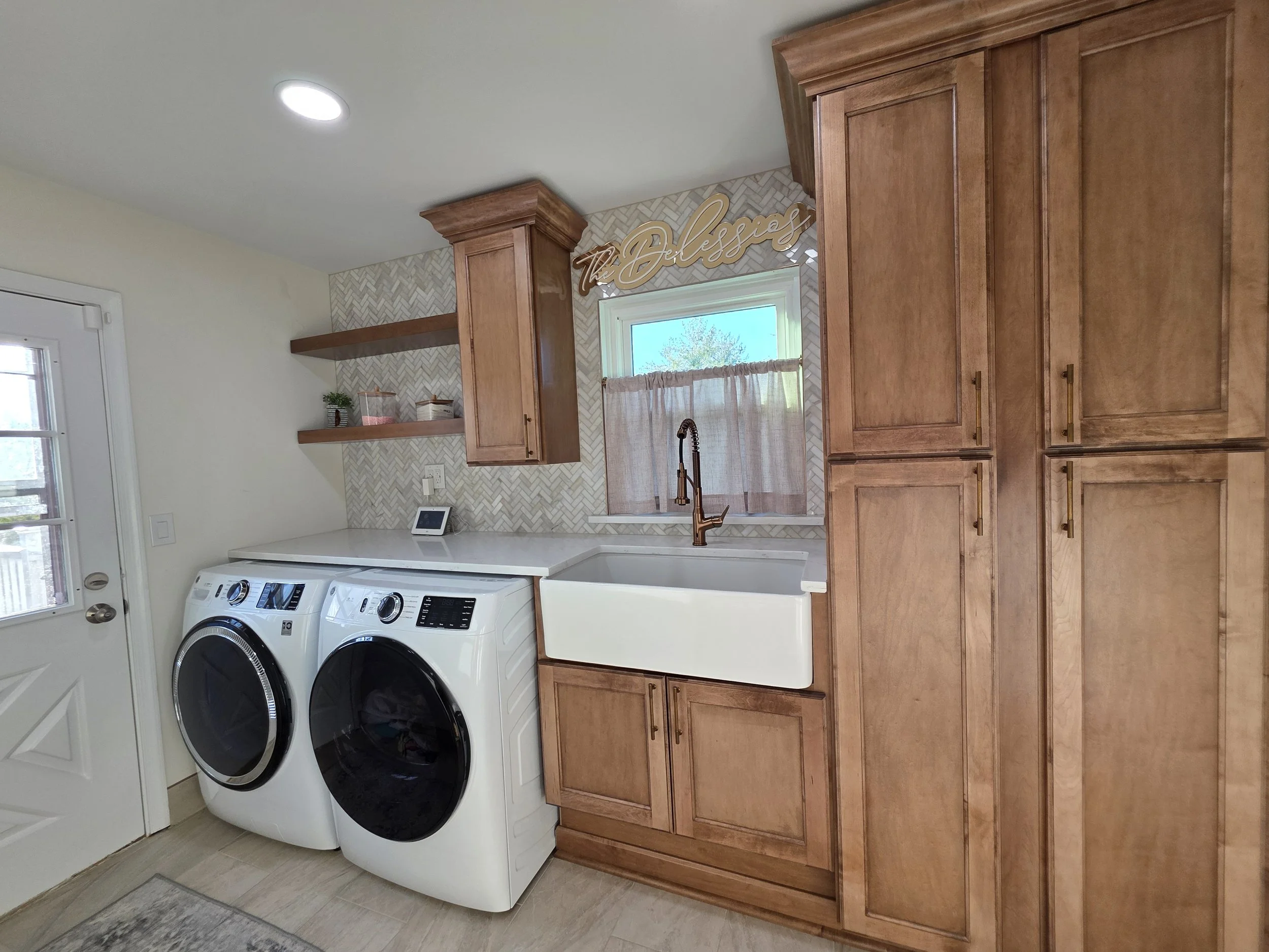 Vinny and Francesca’s remodeled laundry room with wood cabinets, front-loading appliances and a farmhouse sink.