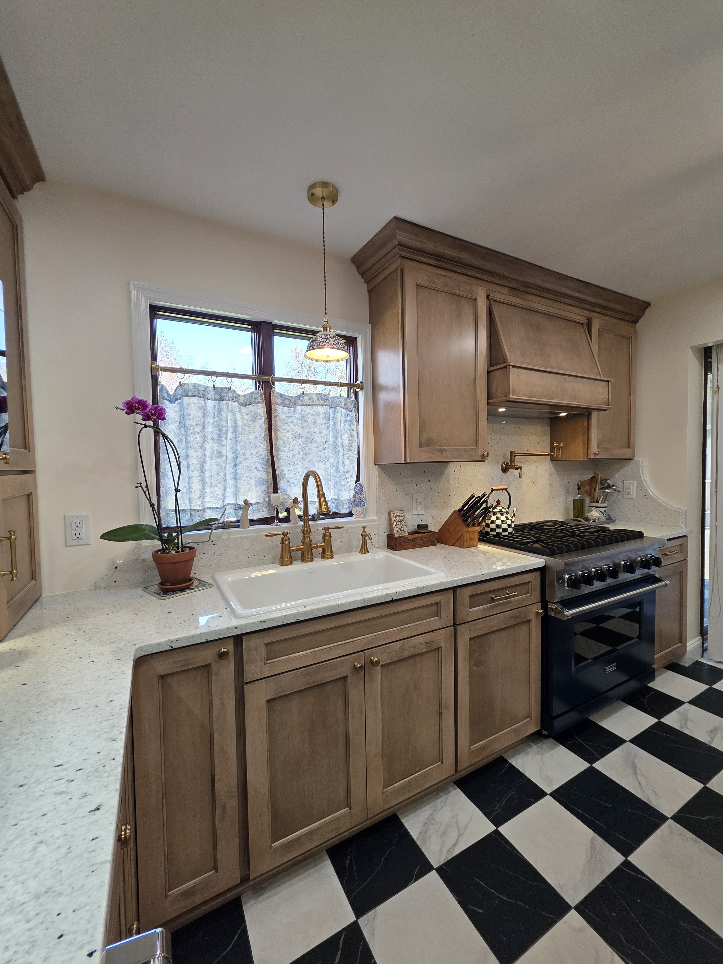 Farmhouse sink beneath the window beside the range and wood cabinetry.