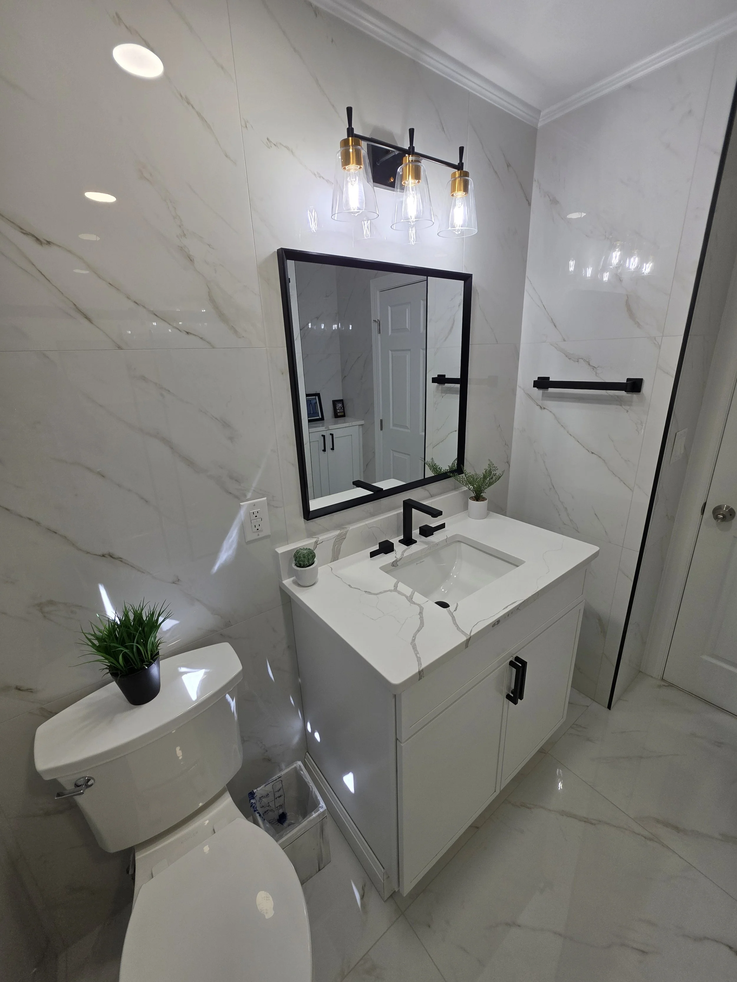 Gray vanity with a white sink, black faucet and rectangular mirror in Samuel’s remodeled hallway bathroom.