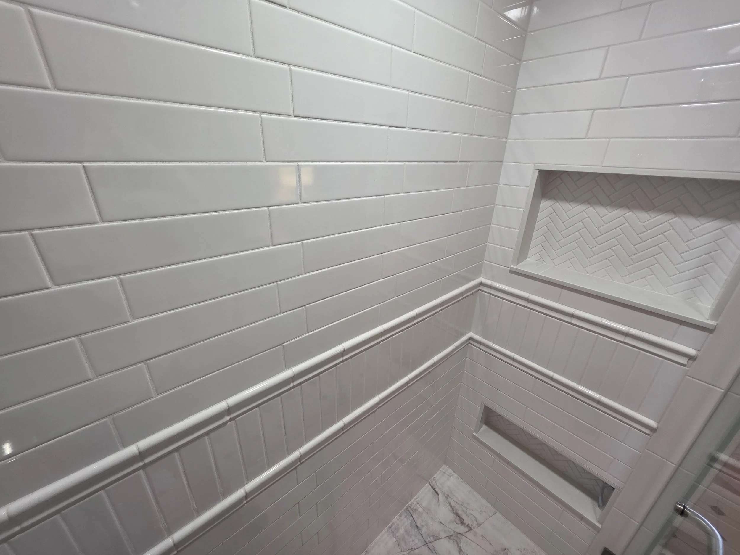 White shower tile with panel trim and recessed niche.