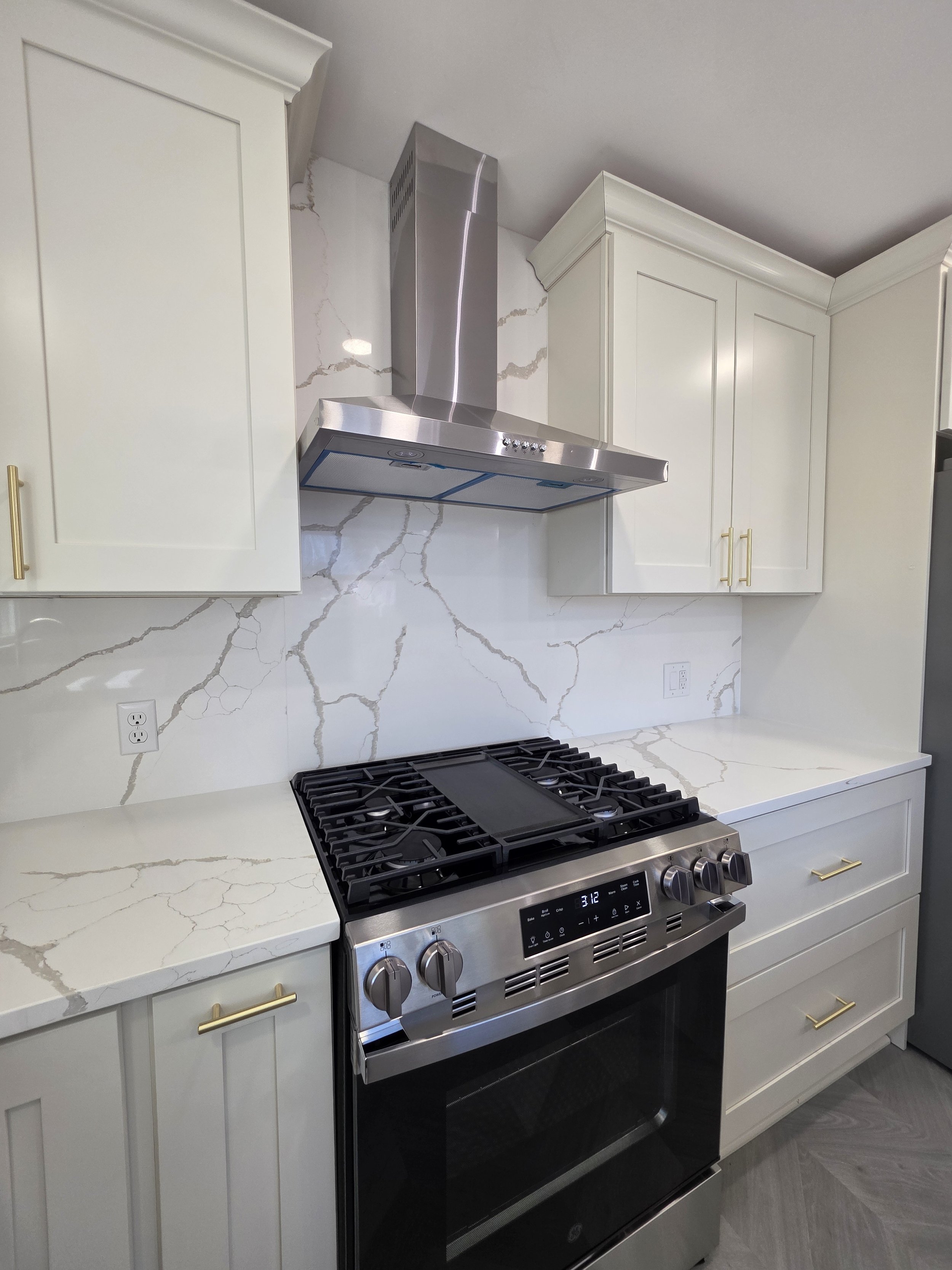Stainless range and chimney hood framed by white cabinets and veined backsplash.