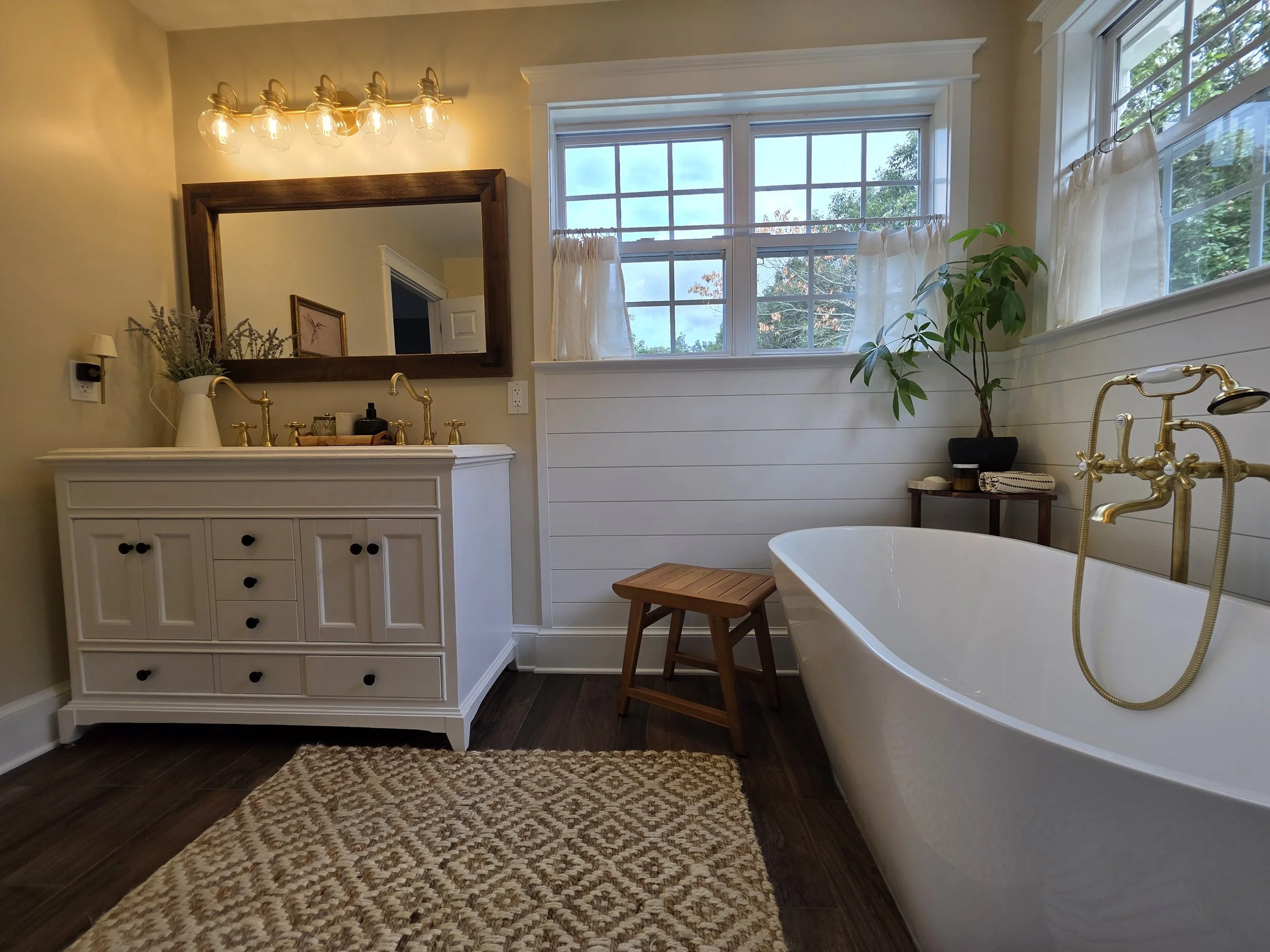 Freestanding bathtub beside classic vanity and bright windows.